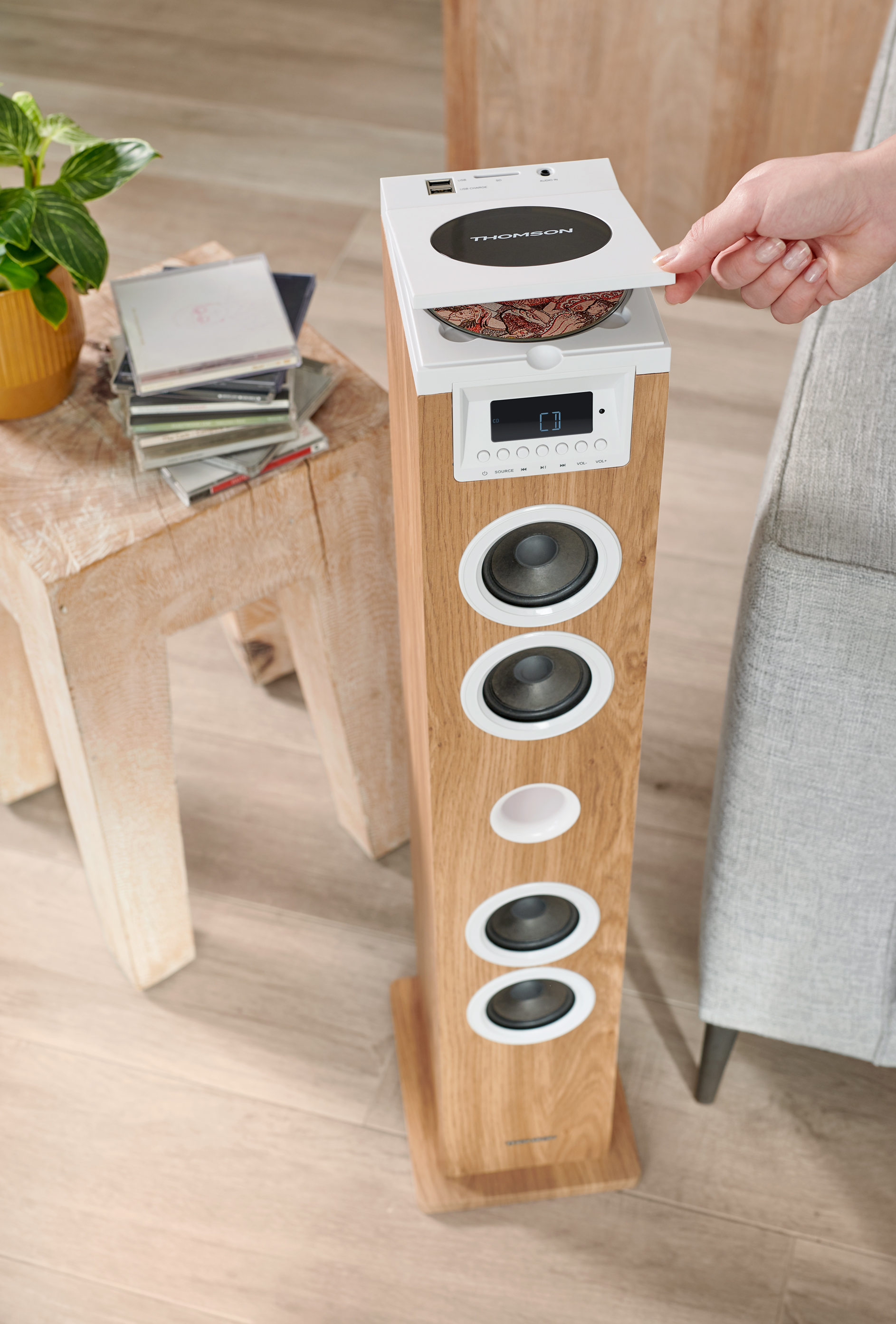 Drewniany głośnik z odtwarzaczem CD na górze. Ręka otwiera tackę CD. Płyty CD na stole.