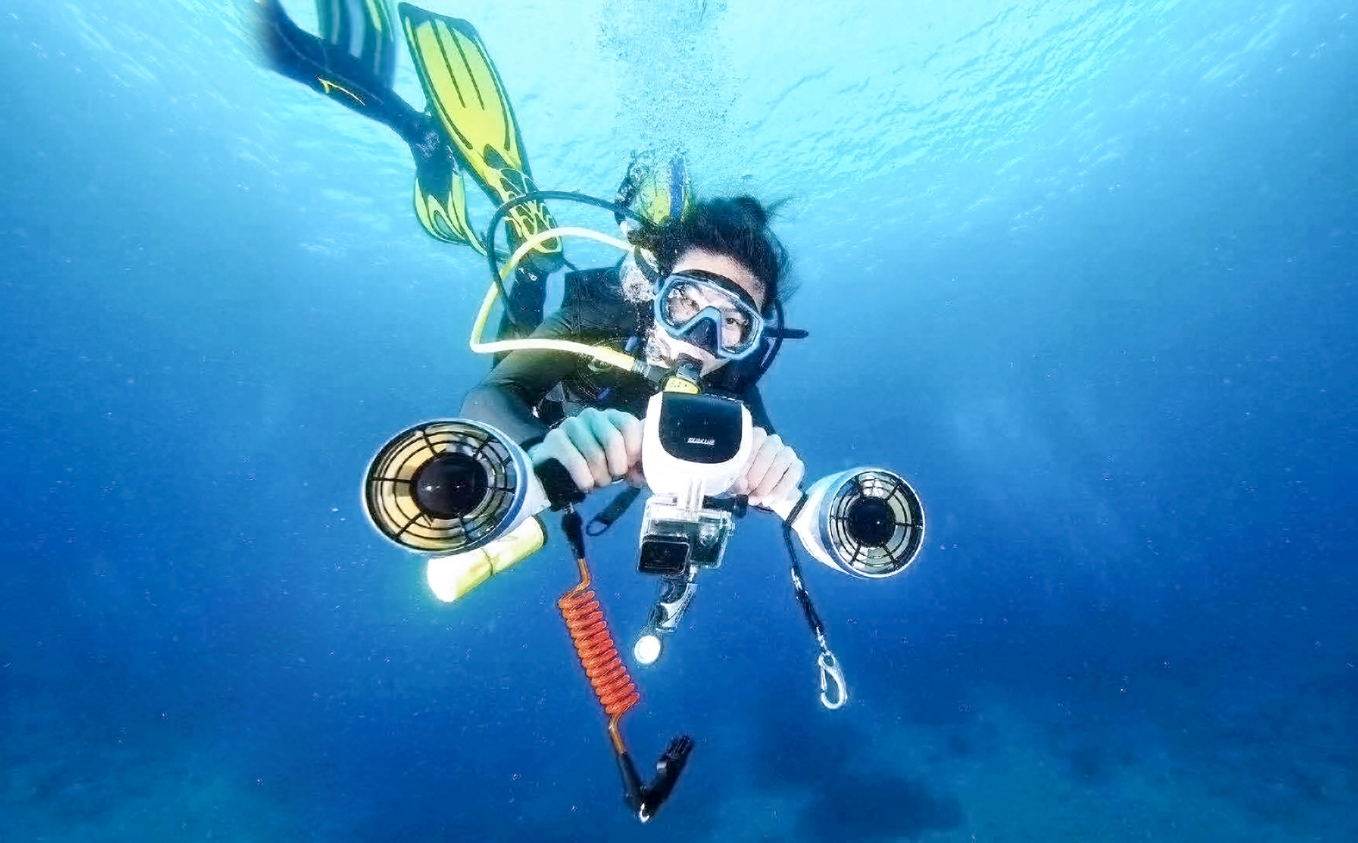 A scuba diver wearing a mask and fins is in the water. He is holding a underwater scooter.