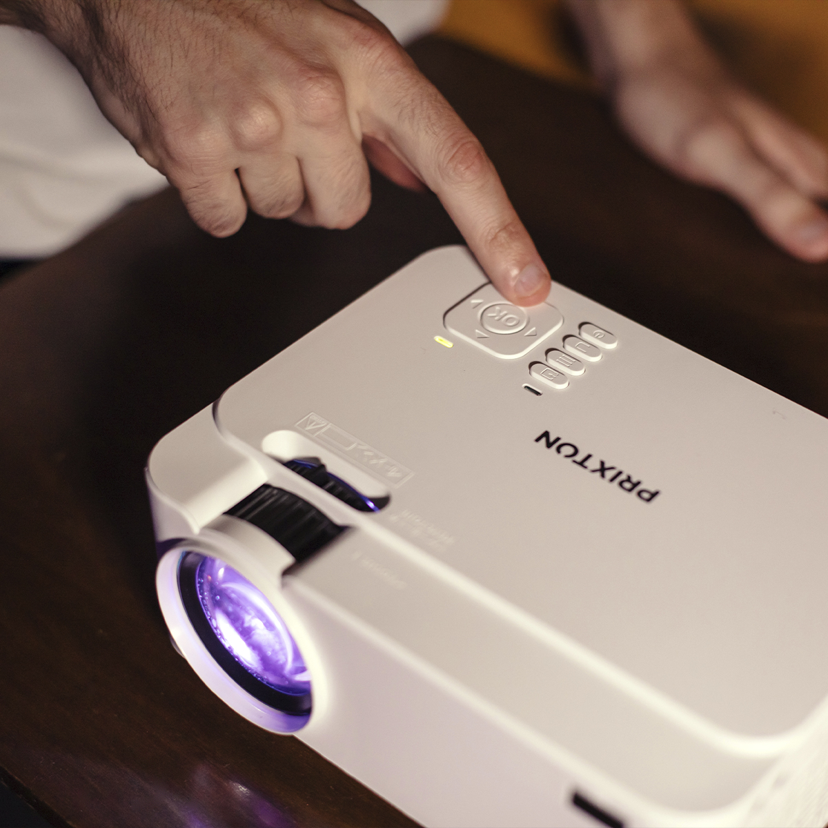 Palec naciska przycisk zasilania na białym projektorze. Obiektyw świeci.