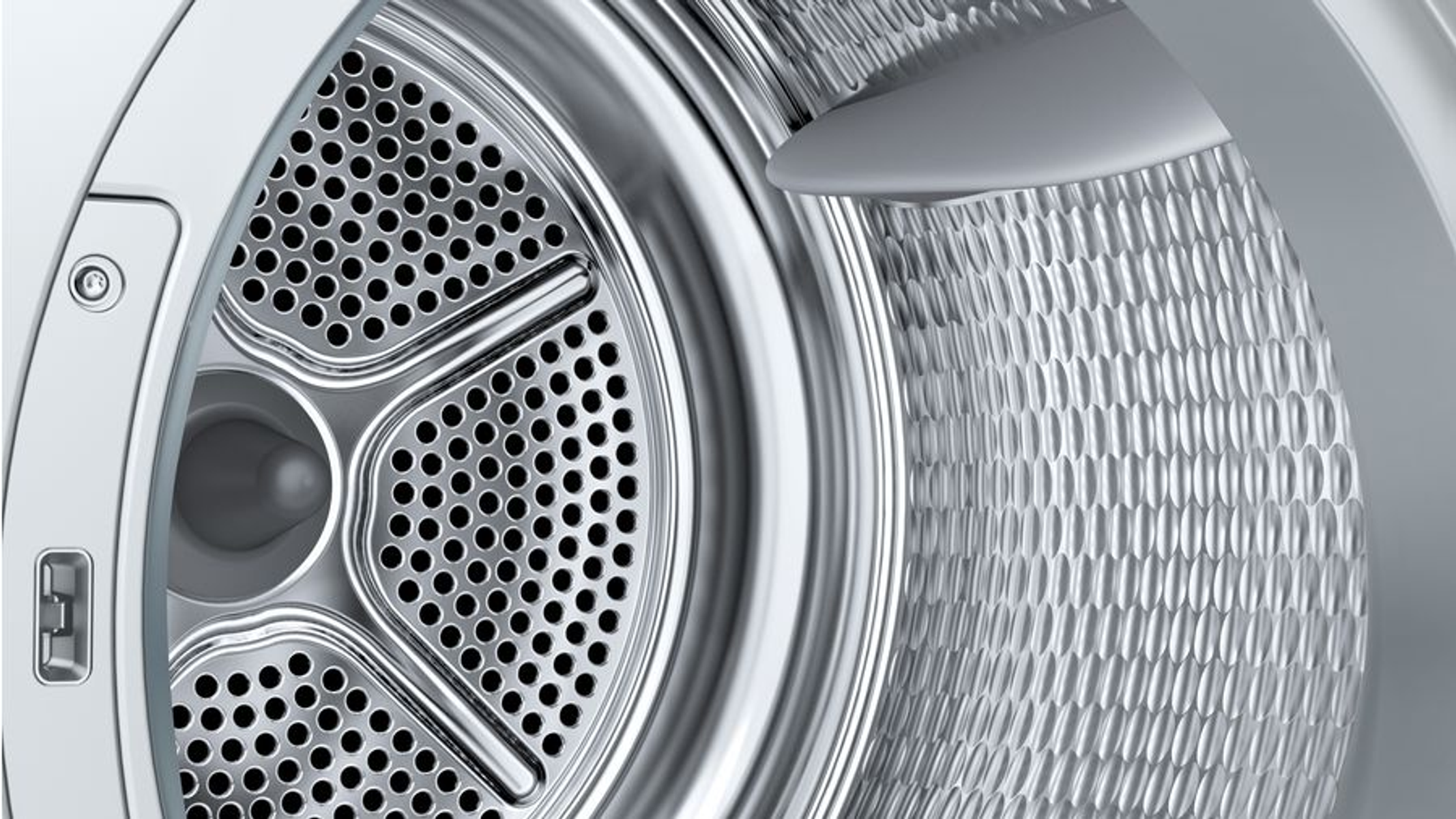 Primo piano dell'interno del cestello di una lavatrice in acciaio inox. Superfici perforate.