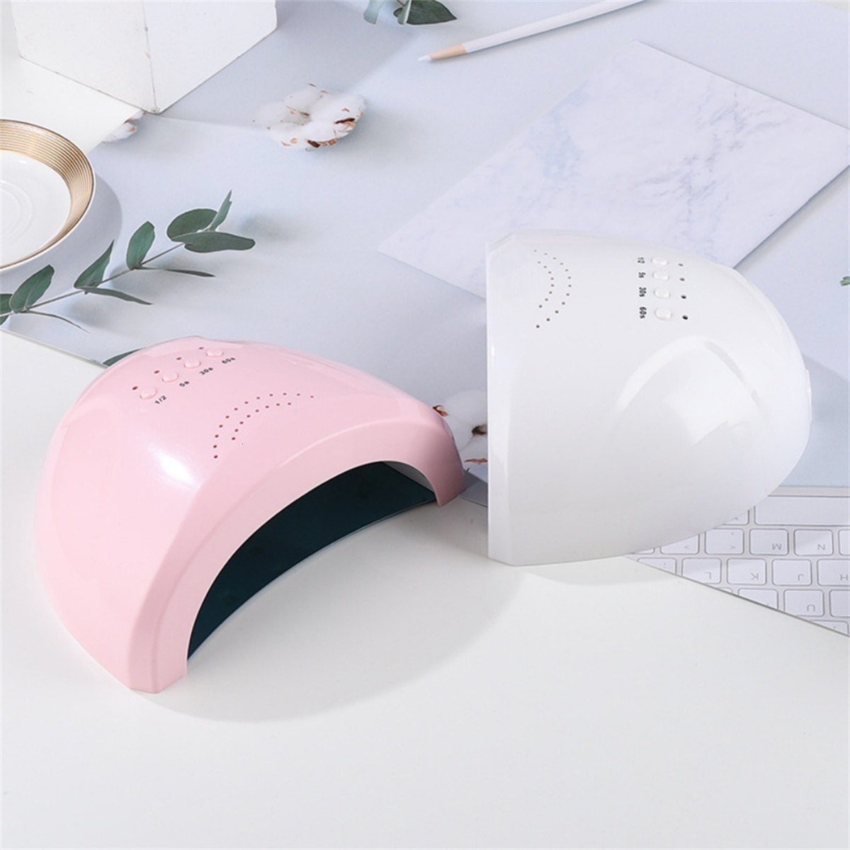 Zwei UV-Nagellampen, rosa und weiß, auf weißer Oberfläche.