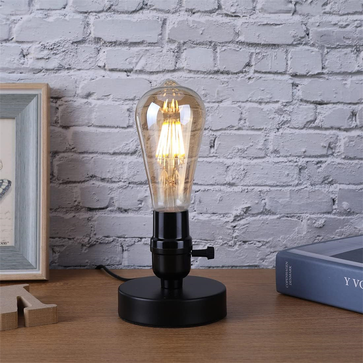 Glühbirnenlampe im Vintage-Stil mit schwarzem Sockel, neben einem Buch.
