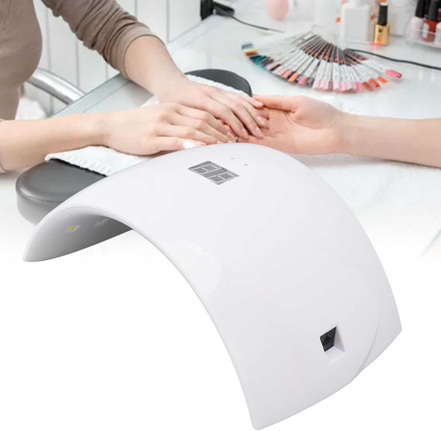 Eine weiße Nagelhärtungslampe mit Digitalanzeige. Hände sind unter der Lampe.