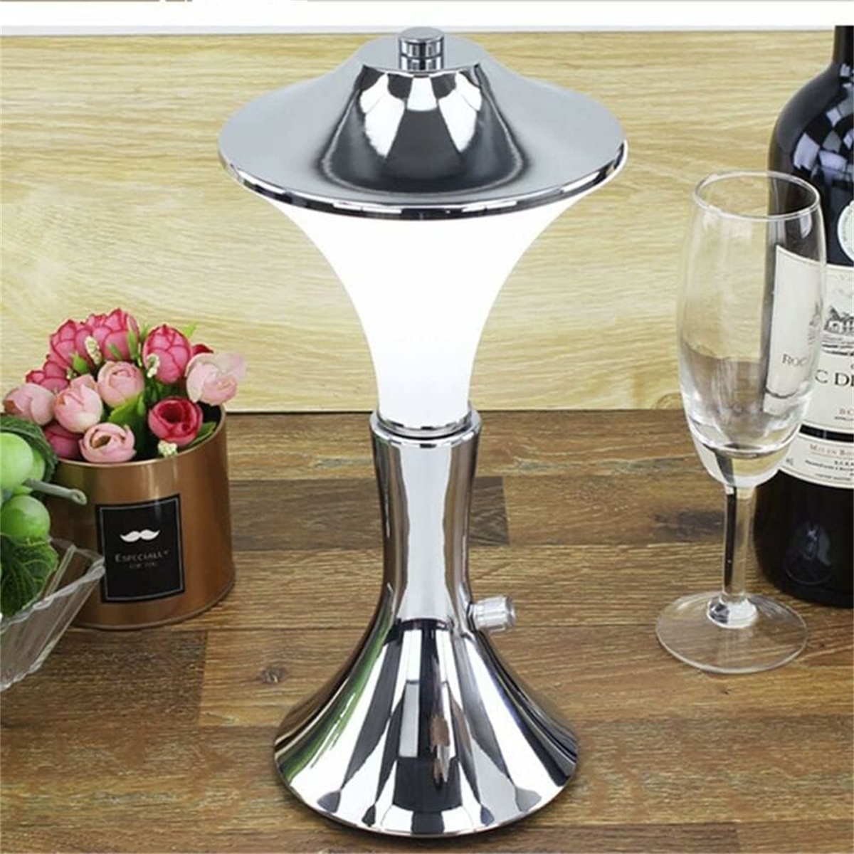 Silberne Lampe auf Holztisch. Weinflasche, Glas und Blumen im Hintergrund.