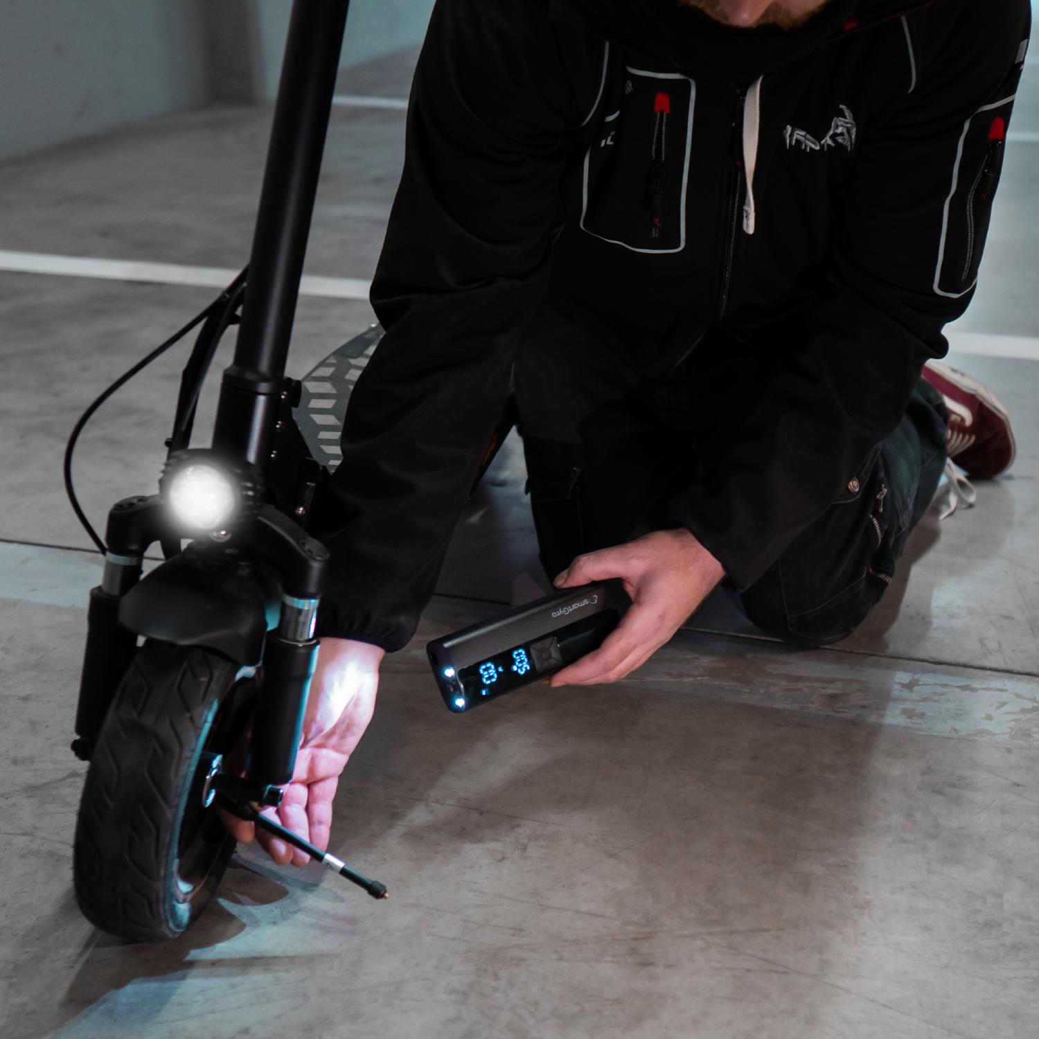 Hombre comprobando la presión de los neumáticos de un patinete eléctrico. Sostiene un dispositivo con números.
