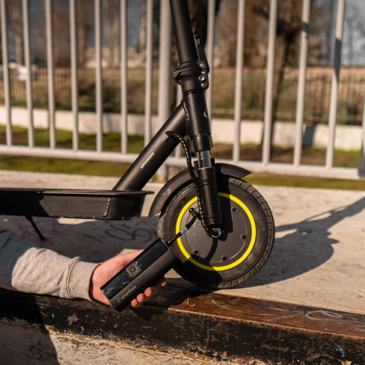 Una persona bombea aire en el neumático de un patinete eléctrico negro con una bomba manual.