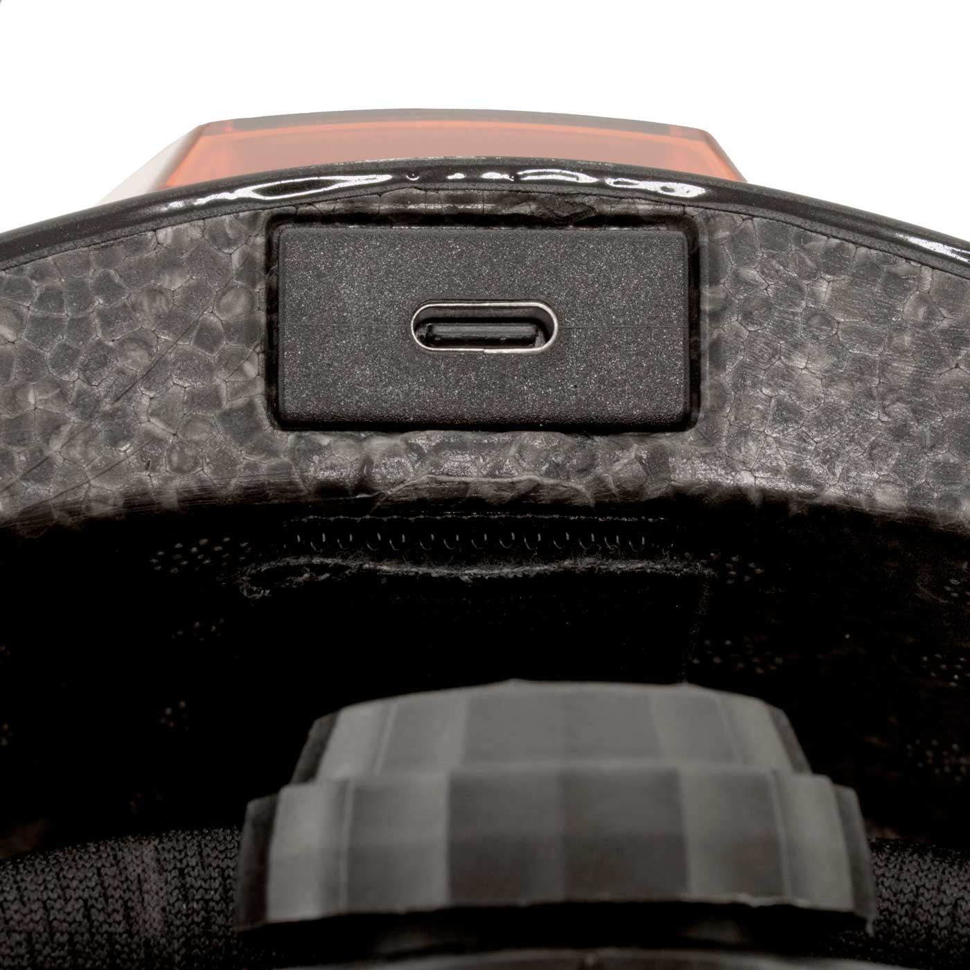 Primer plano de un casco negro con un puerto USB-C. Una luz roja y una perilla son visibles.