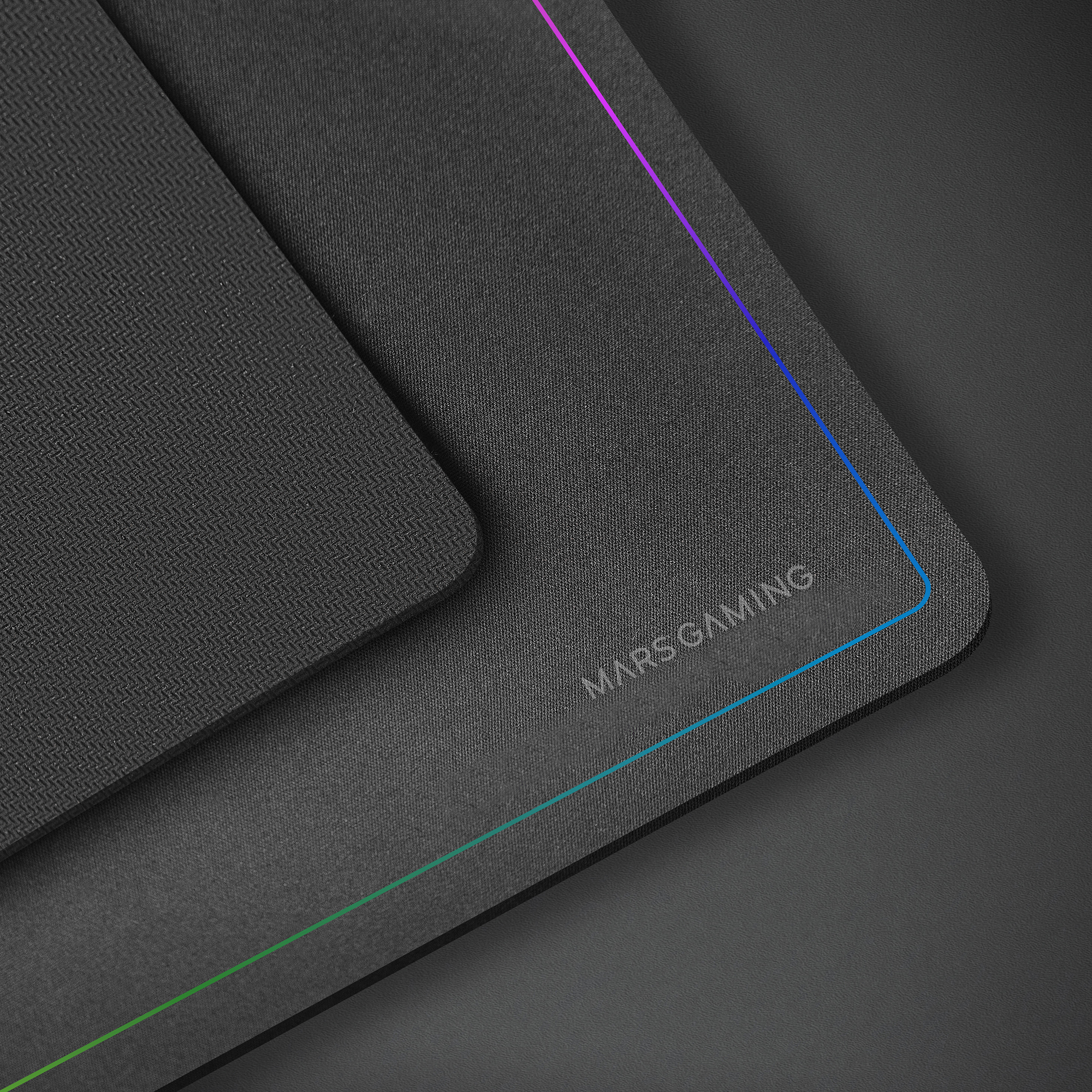 Zbliżenie podkładki pod mysz dla graczy. Ma czarną powierzchnię z napisem MARS GAMING i kolorową linią na krawędzi.