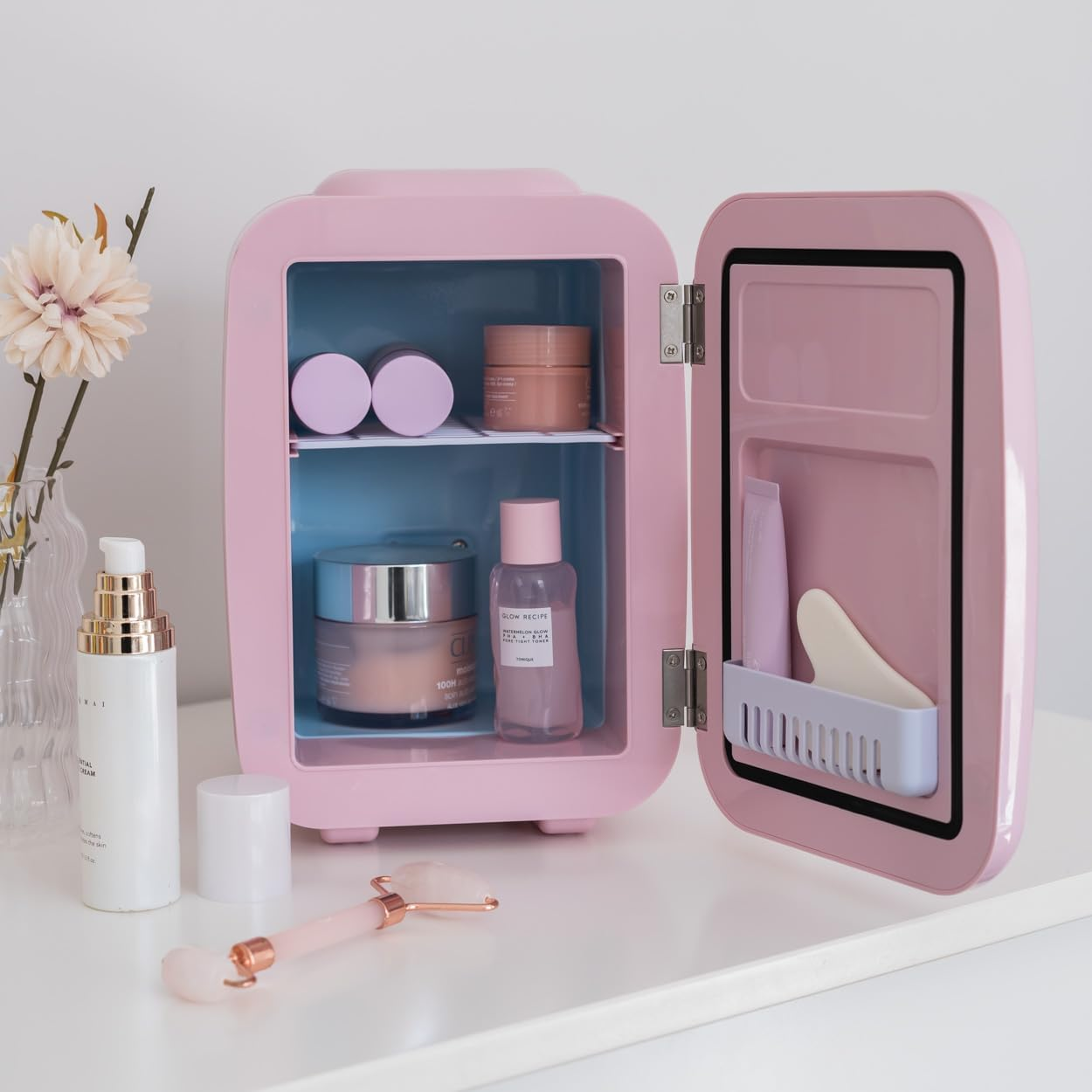 Mini-nevera rosa abierta, llena de productos para el cuidado de la piel, sobre una superficie blanca.