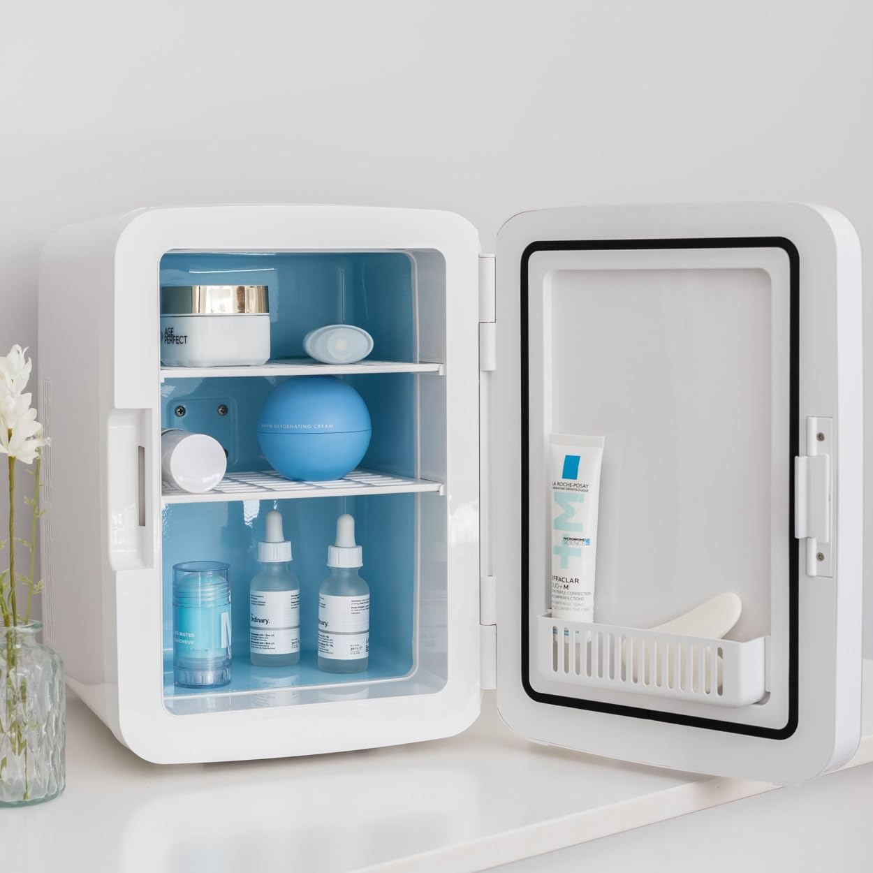 Una mini nevera blanca con cosméticos dentro, interior azul.