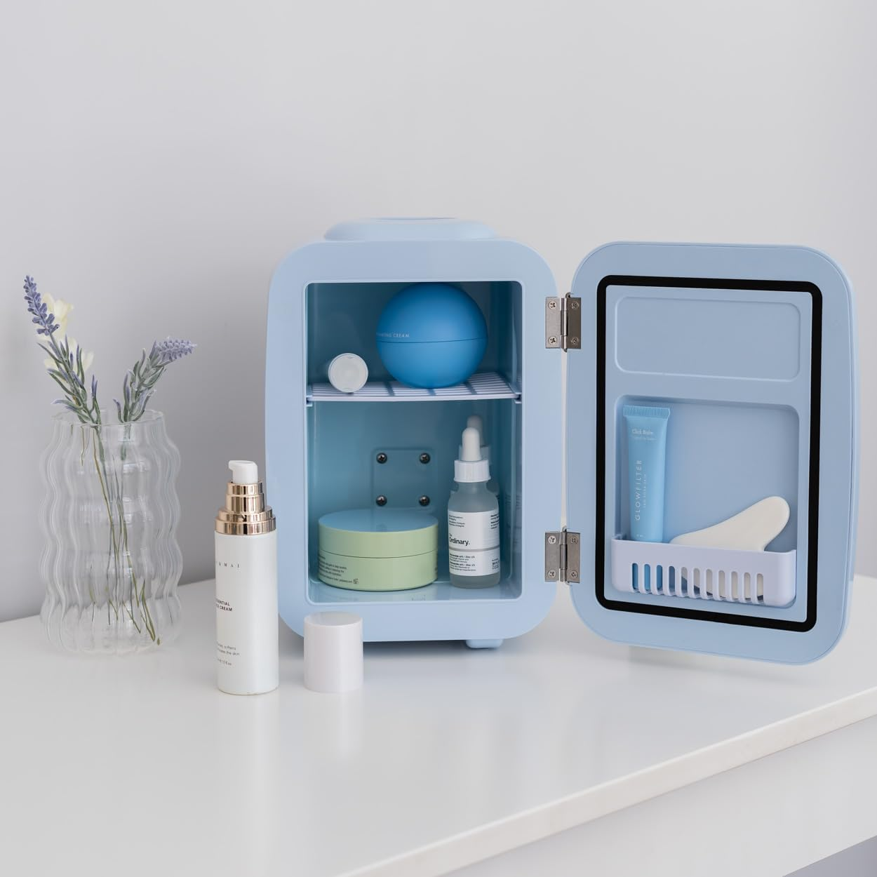 Una mini nevera con cosméticos y productos para el cuidado de la piel dentro y sobre la mesa.