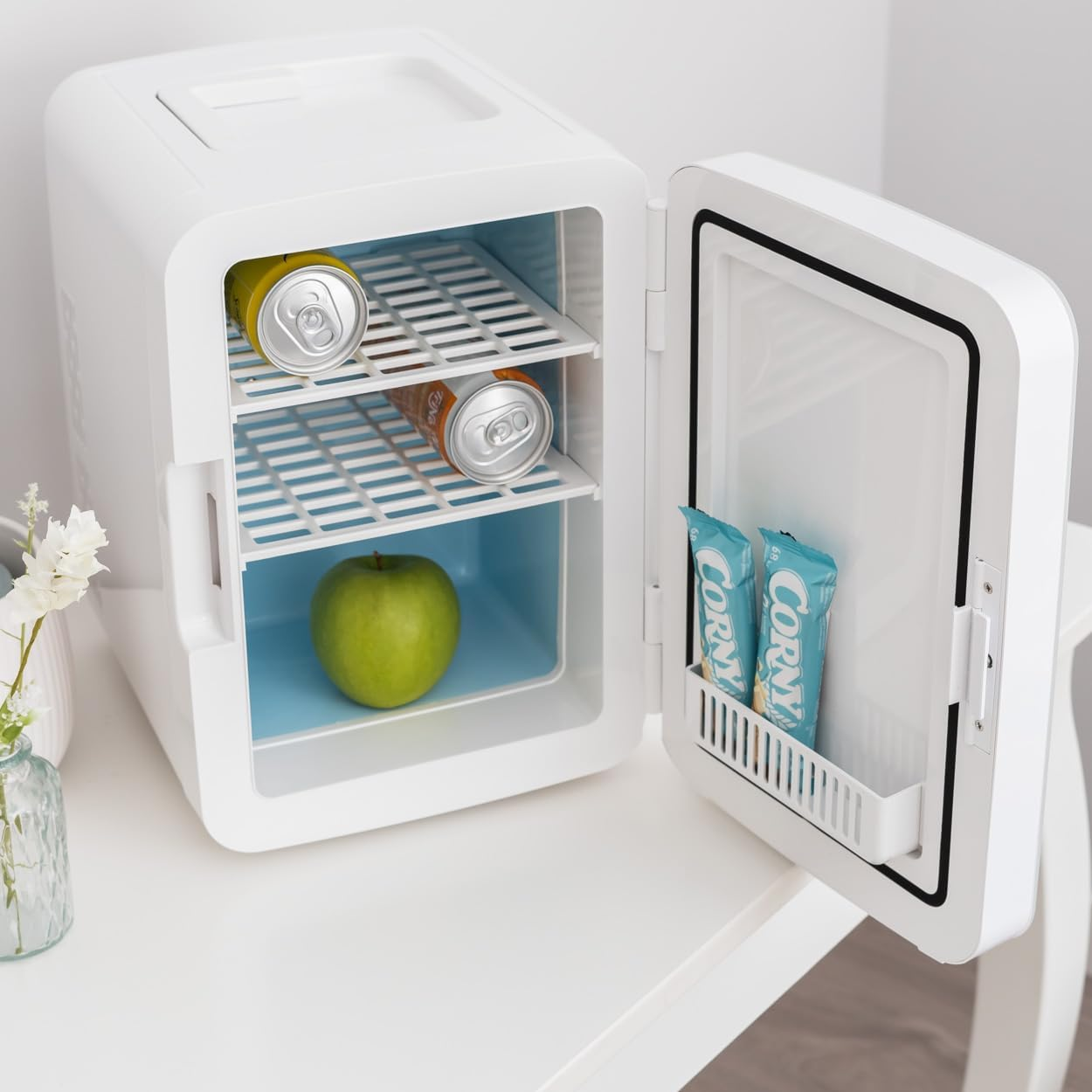 Min nevera blanca, abierta. Contiene latas, una manzana y snacks. La puerta está abierta.