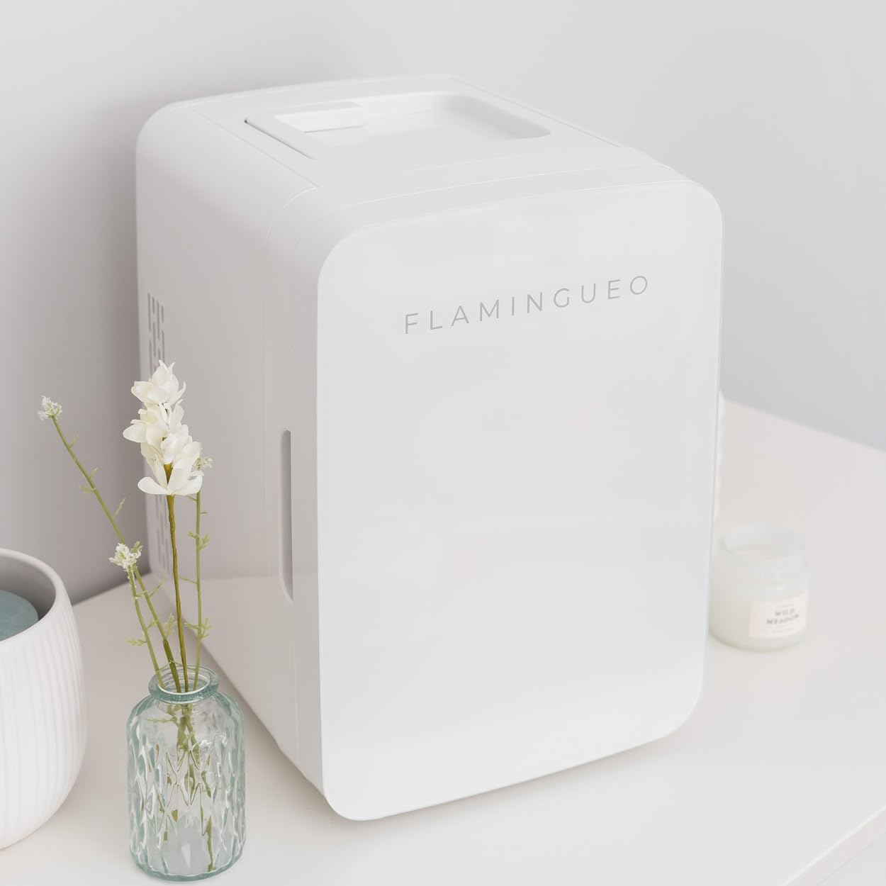 Nevera blanca en una mesa blanca junto a un jarrón con flores y una vela.