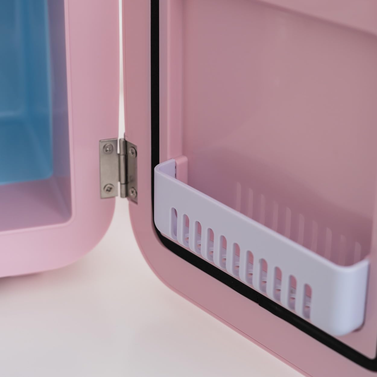 Min nevera rosa con la puerta abierta, revelando un estante blanco y el compartimento azul en su interior.