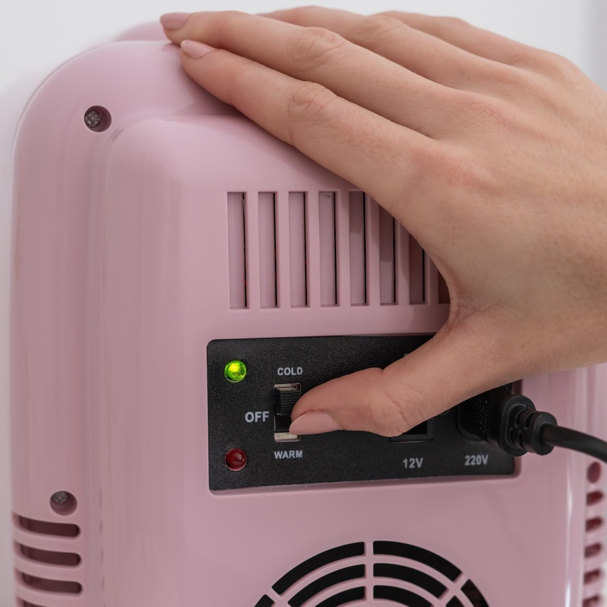 Una mano enciende el botón de encendido de una mini nevera rosa.