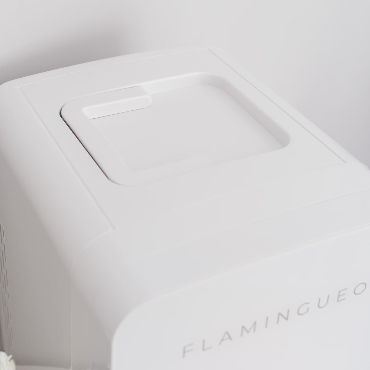 Vista de cerca de un electrodoméstico blanco. La parte superior tiene una abertura rectangular. La palabra 'FLAMINGUEO' es visible.