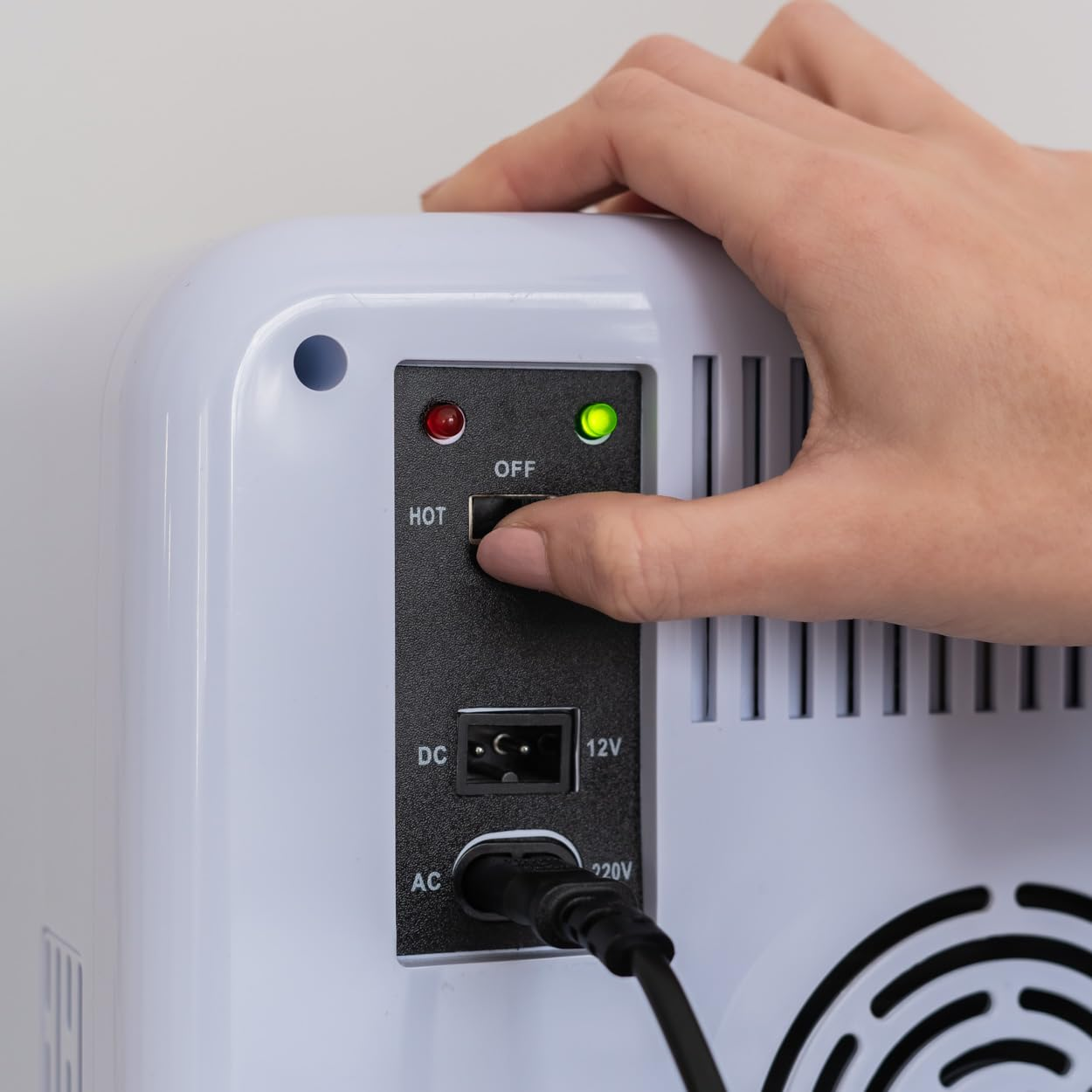 Una mano enciende un interruptor de apagado a encendido, con luz verde. Nevera blanca.