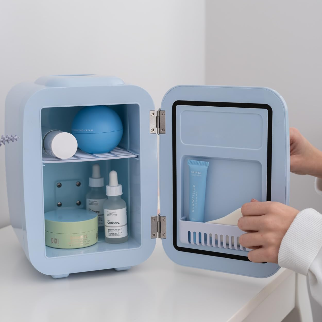 Una mini nevera azul claro con productos para el cuidado de la piel dentro, y una mano que se mete.