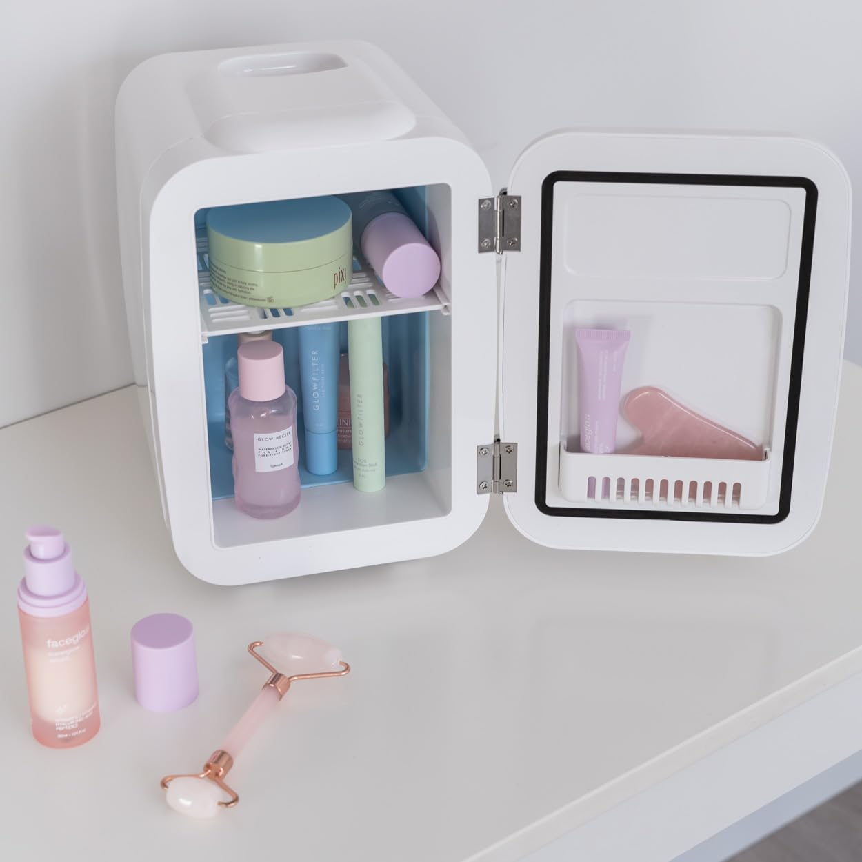Pequeño frigorífico blanco abierto, con productos para el cuidado de la piel dentro. Maquillaje y rodillo.