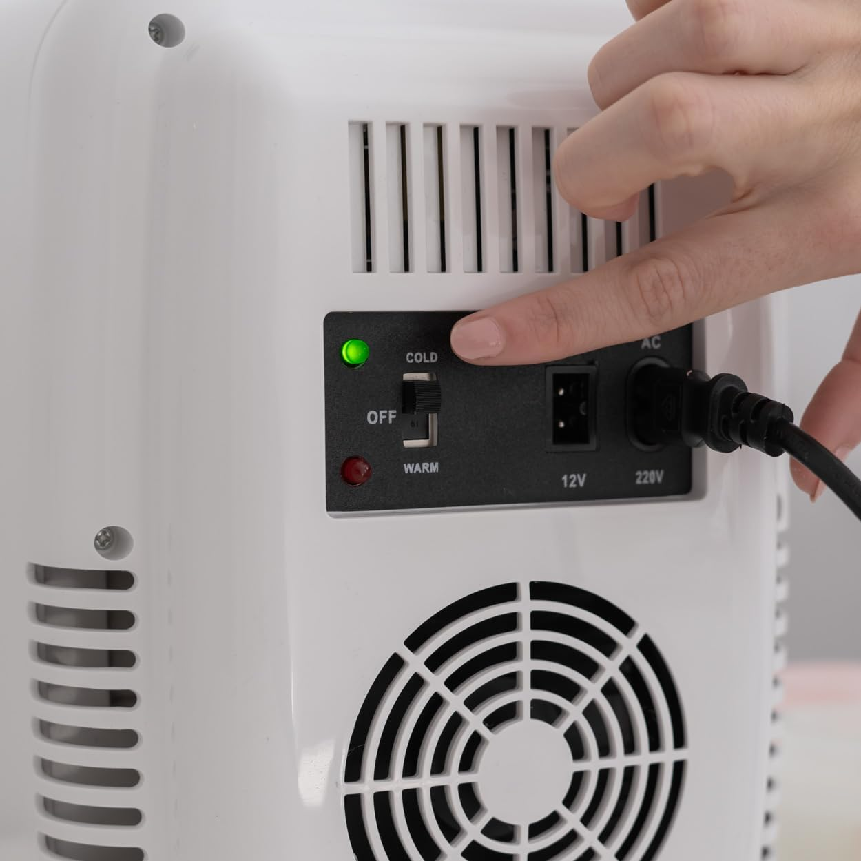Una mano presionando un botón en una mini nevera blanca, mostrando el panel de control.