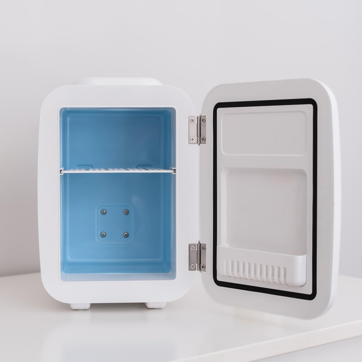 Mini-nevera blanca con la puerta abierta, mostrando un interior azul. Sobre una superficie blanca.