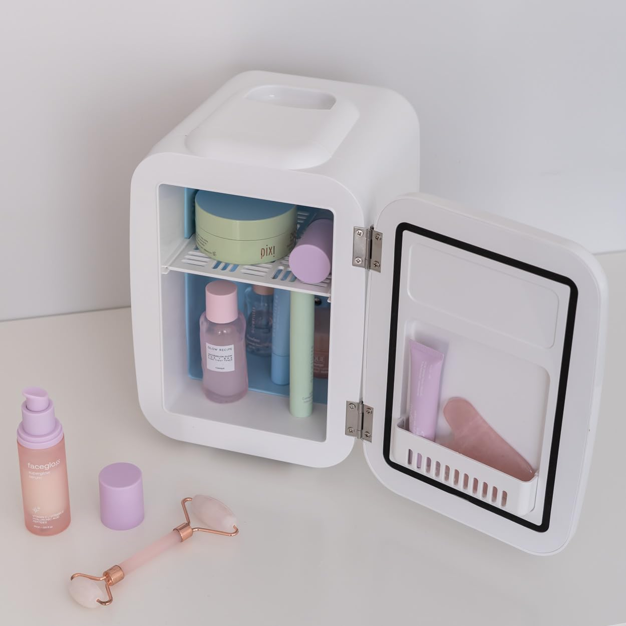 Mini-nevera blanca abierta, con productos de belleza dentro y sobre la mesa.