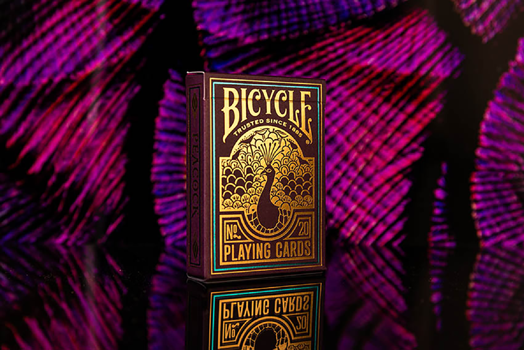 Bicycle Spielkartenbox. Dunkelviolette Box mit goldenen Details, einer Pfauenillustration und Logo.