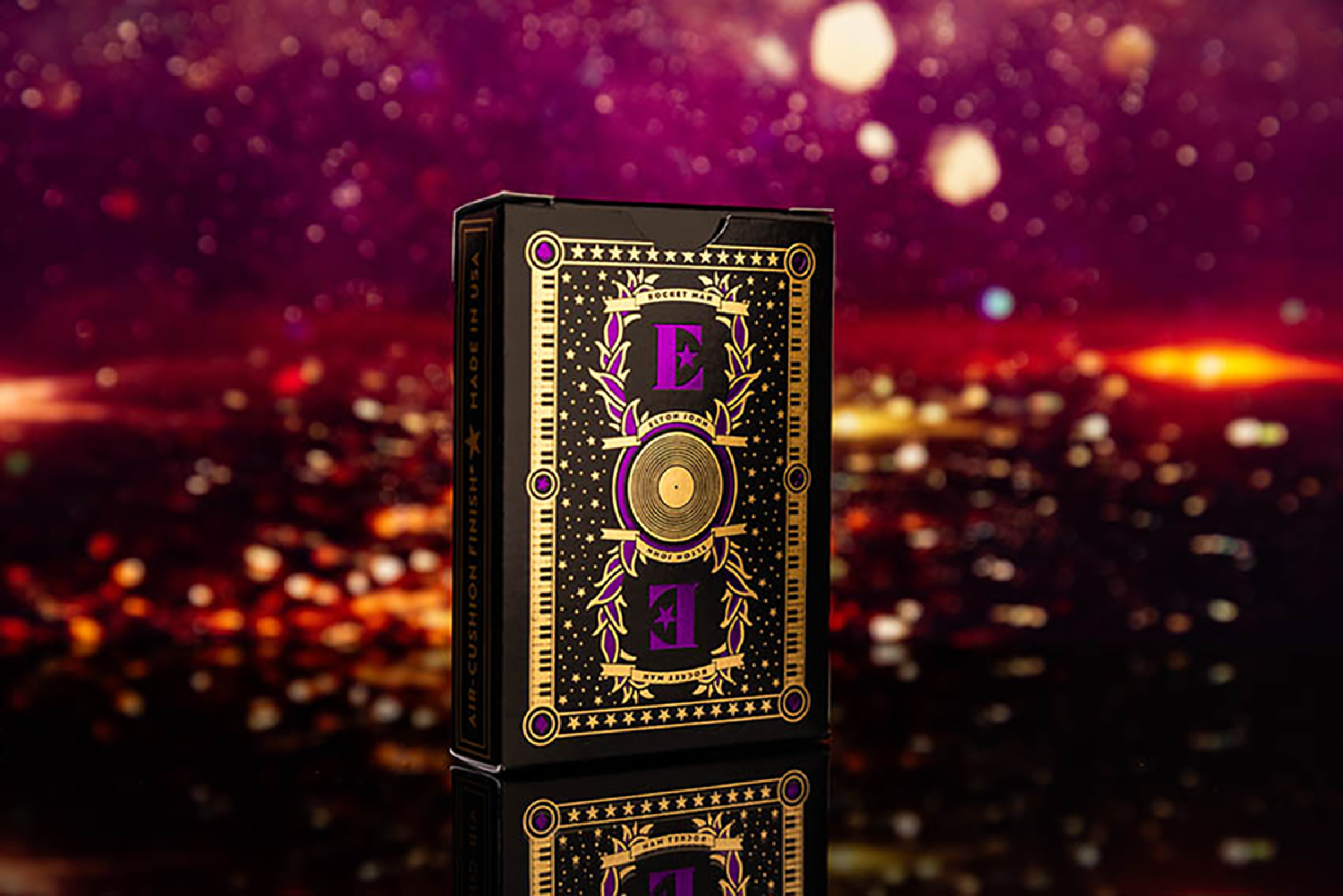 Eine schwarze Spielkartenbox mit goldenem und lila Design, vor verschwommenem Stadtbild.