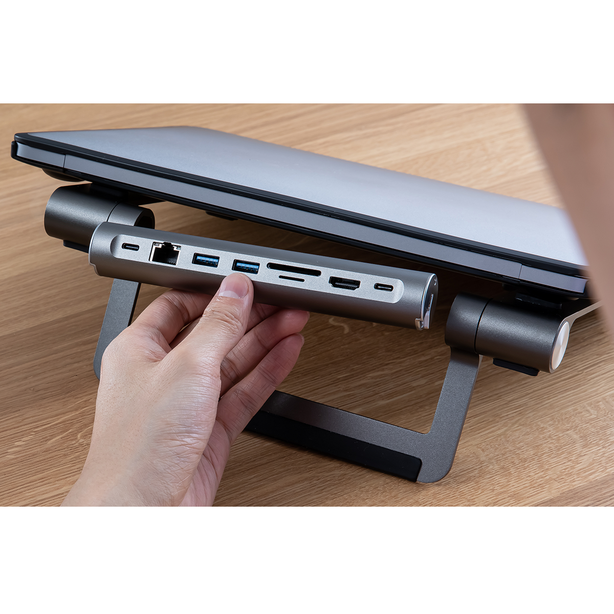Laptop auf silbernem Ständer mit USB-Hub und Hand einer Person.