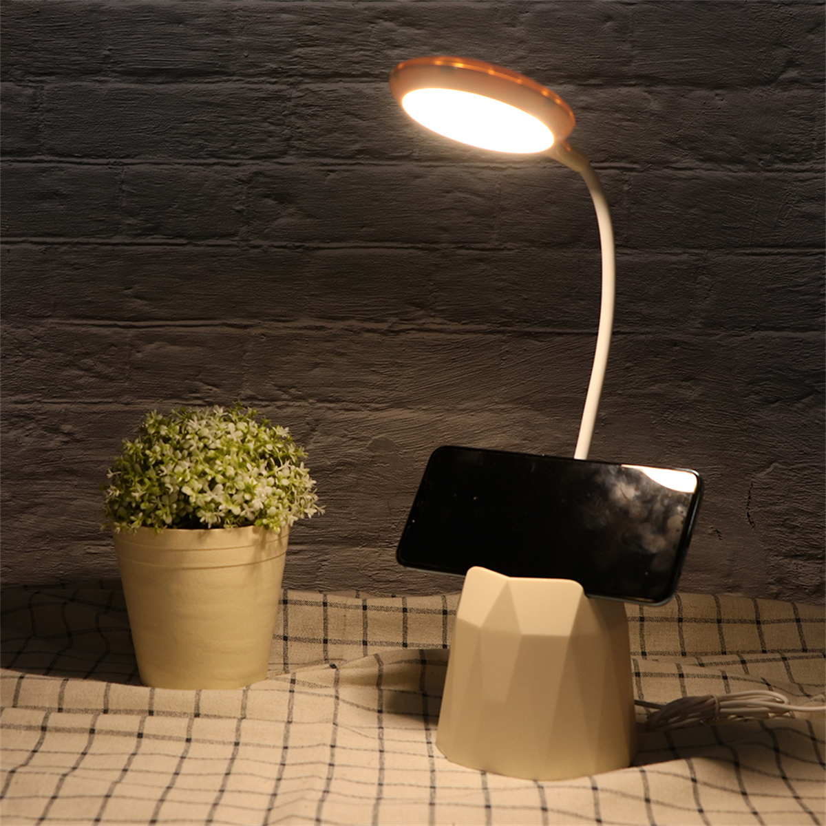 Schreibtischlampe mit Telefon auf Ständer, Pflanze und gemustertem Tuch.