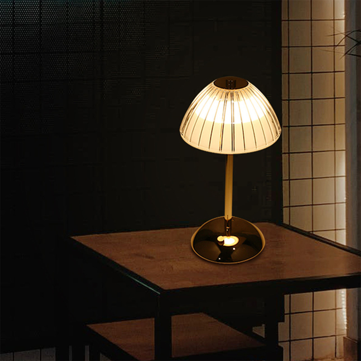 Eine Tischlampe auf einem Holztisch. Sie hat einen goldenen Sockel und einen transparenten, gerippten Lampenschirm.