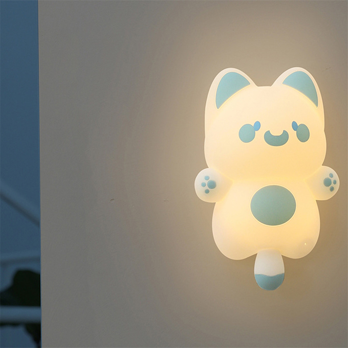 Katzenförmiges Nachtlicht an einer Wand. Es ist weiß, mit blauen Akzenten. Das Licht ist an.