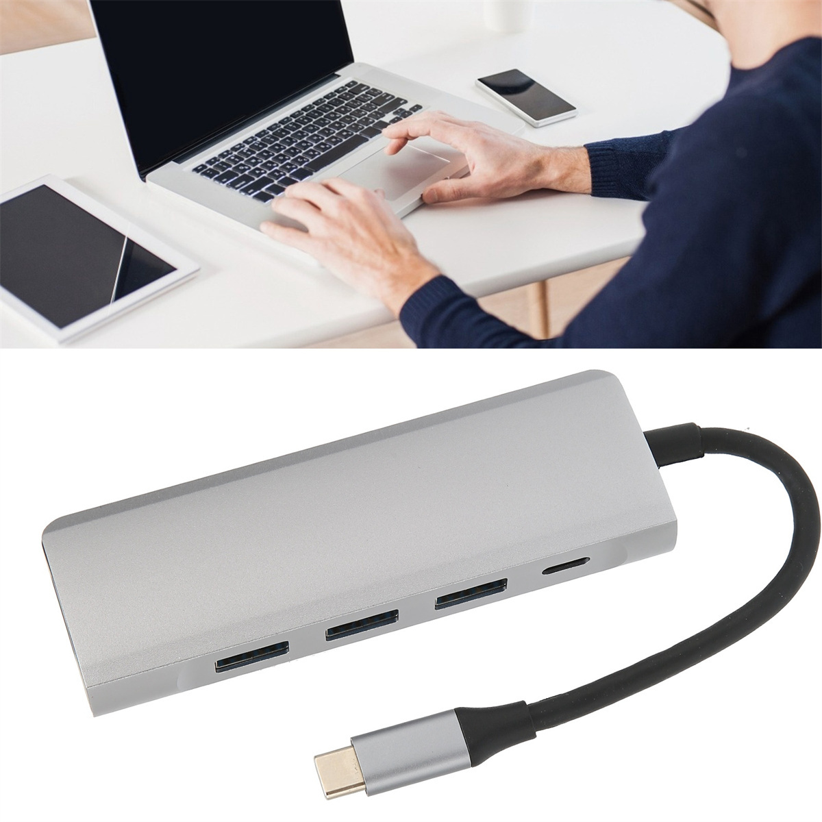 Person benutzt Laptop und einen silbernen Hub mit mehreren Anschlüssen. Der Hub steht auf einem weißen Tisch.