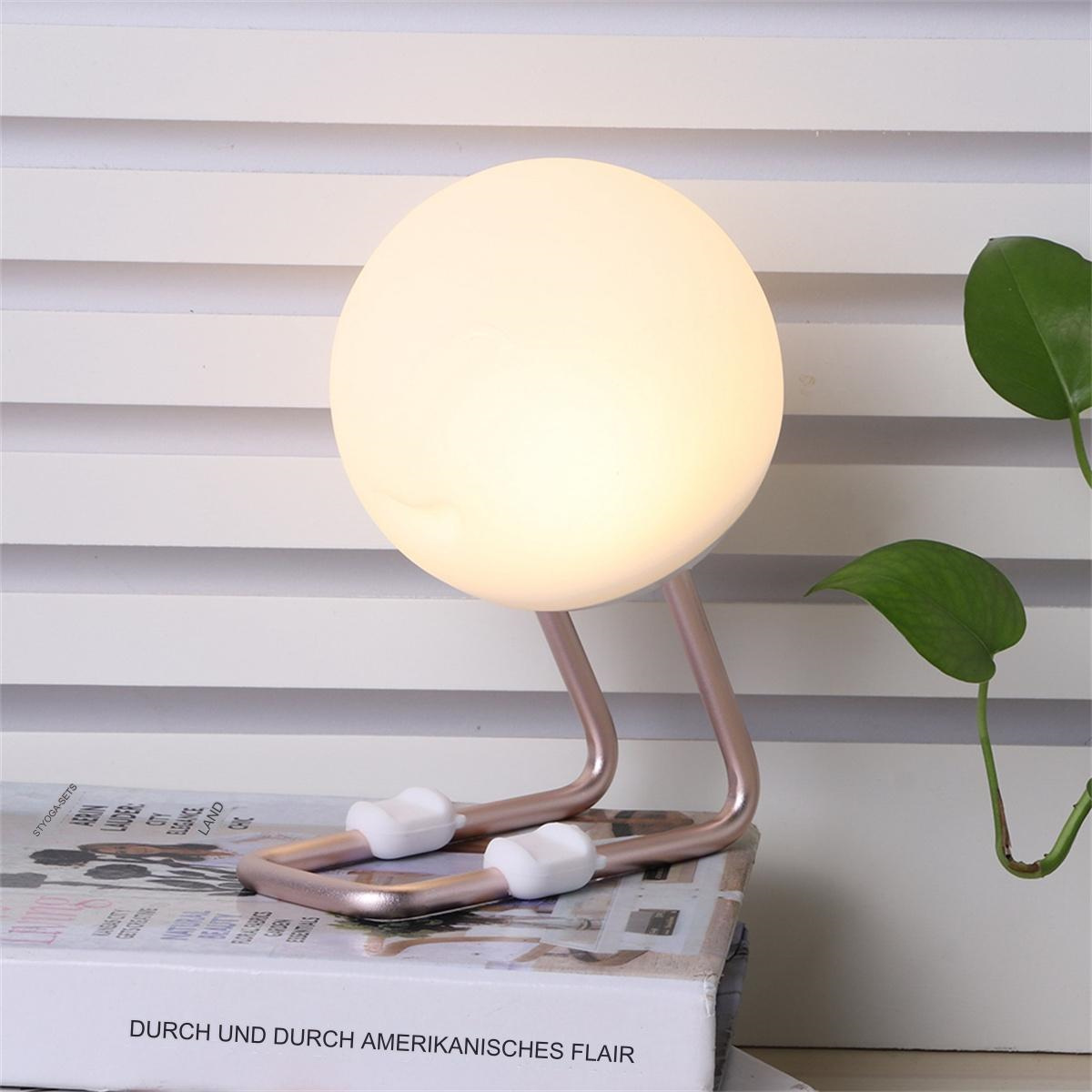 Eine runde, leuchtende Lampe auf einem roségoldenen Rahmen, auf einem Stapel Bücher. Eine Pflanze ist im Hintergrund.