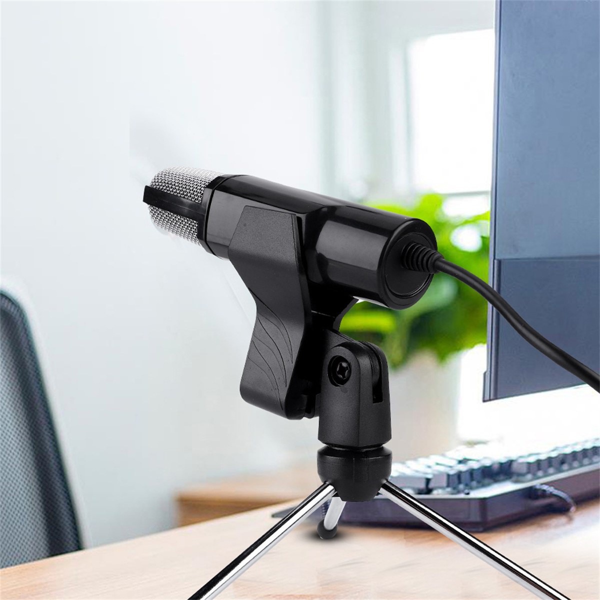 Schwarzes Mikrofon auf einem Stativ, nach links gerichtet, mit einem Computermonitor im Hintergrund.
