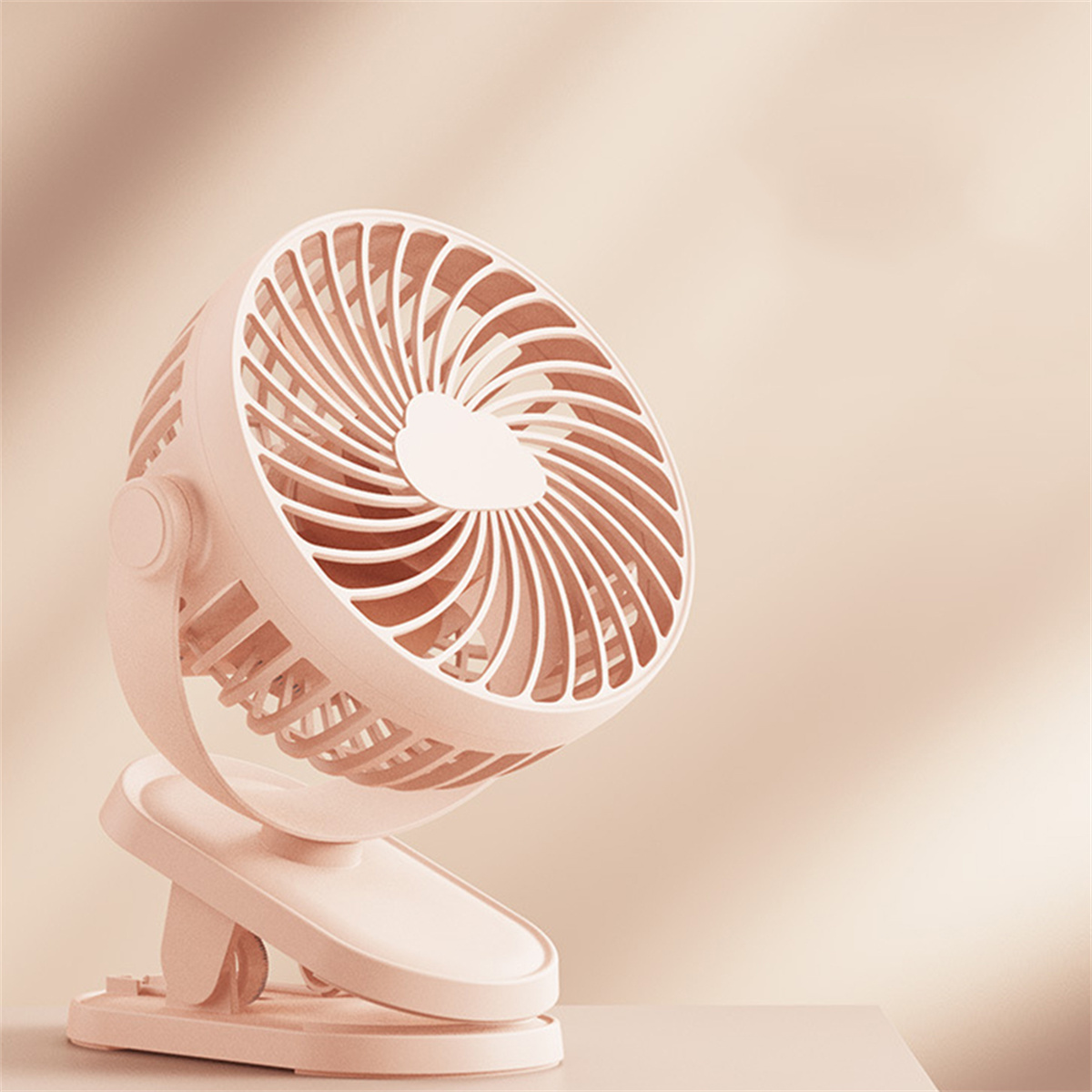 Ein kleiner rosa Schreibtischventilator mit Clipfuß und geschwungenem Design.