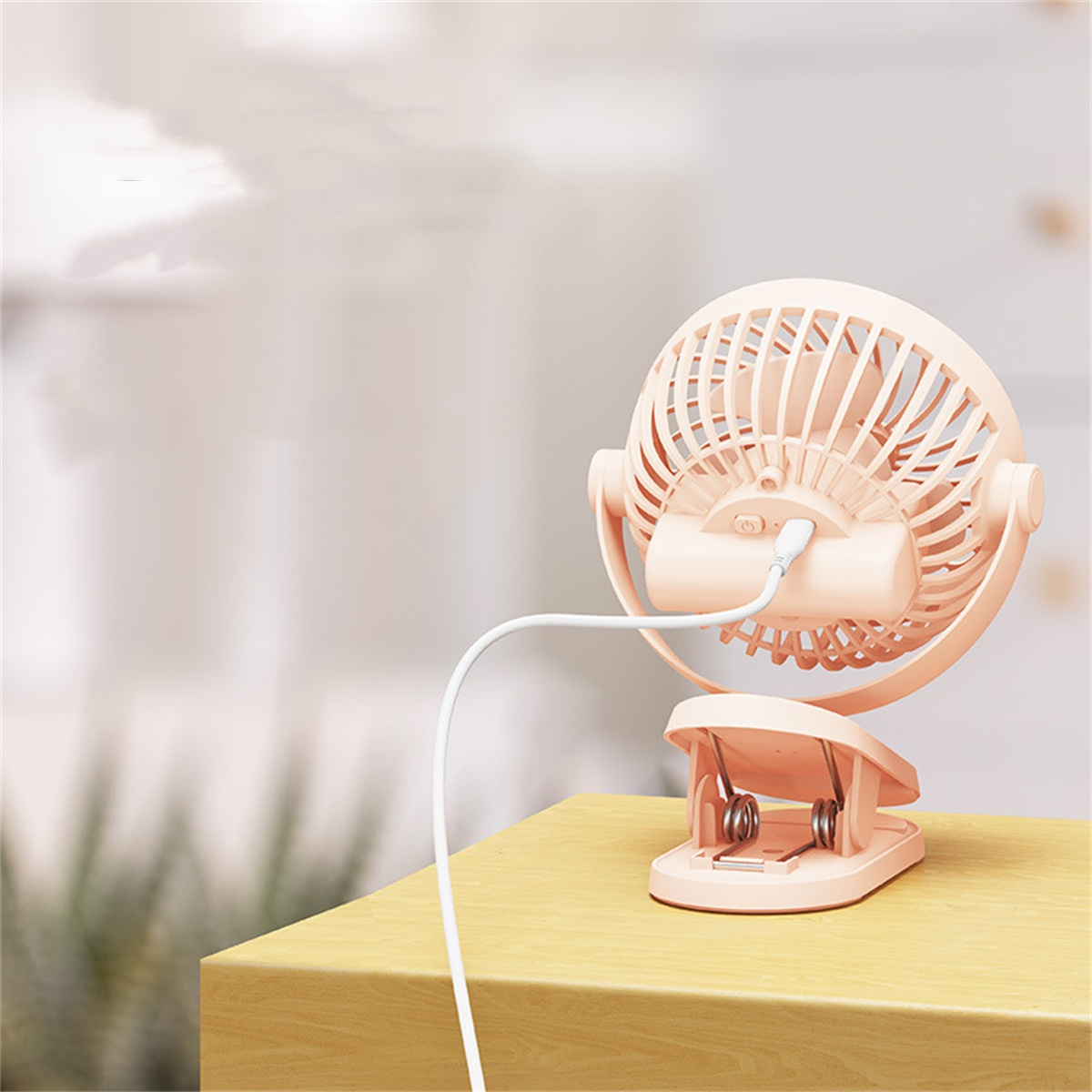 Rosa Mini-Ventilator an einem Holztisch befestigt. Ein weißes Kabel geht vom Ventilator aus.