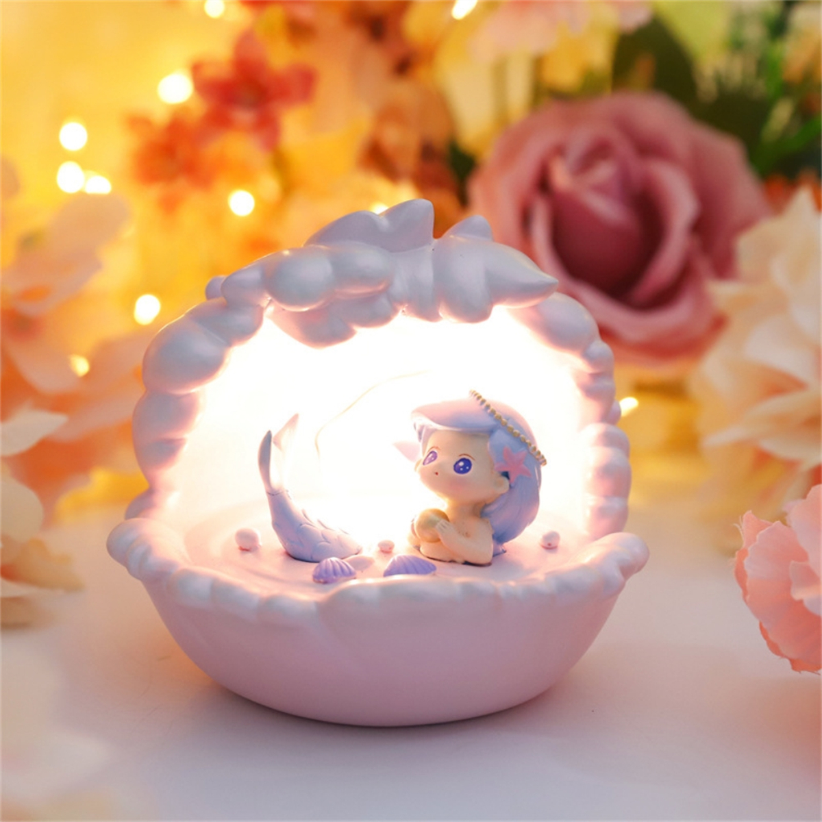 Ein muschelförmiges Nachtlicht mit einer Meerjungfrau darin, umgeben von Blumen.
