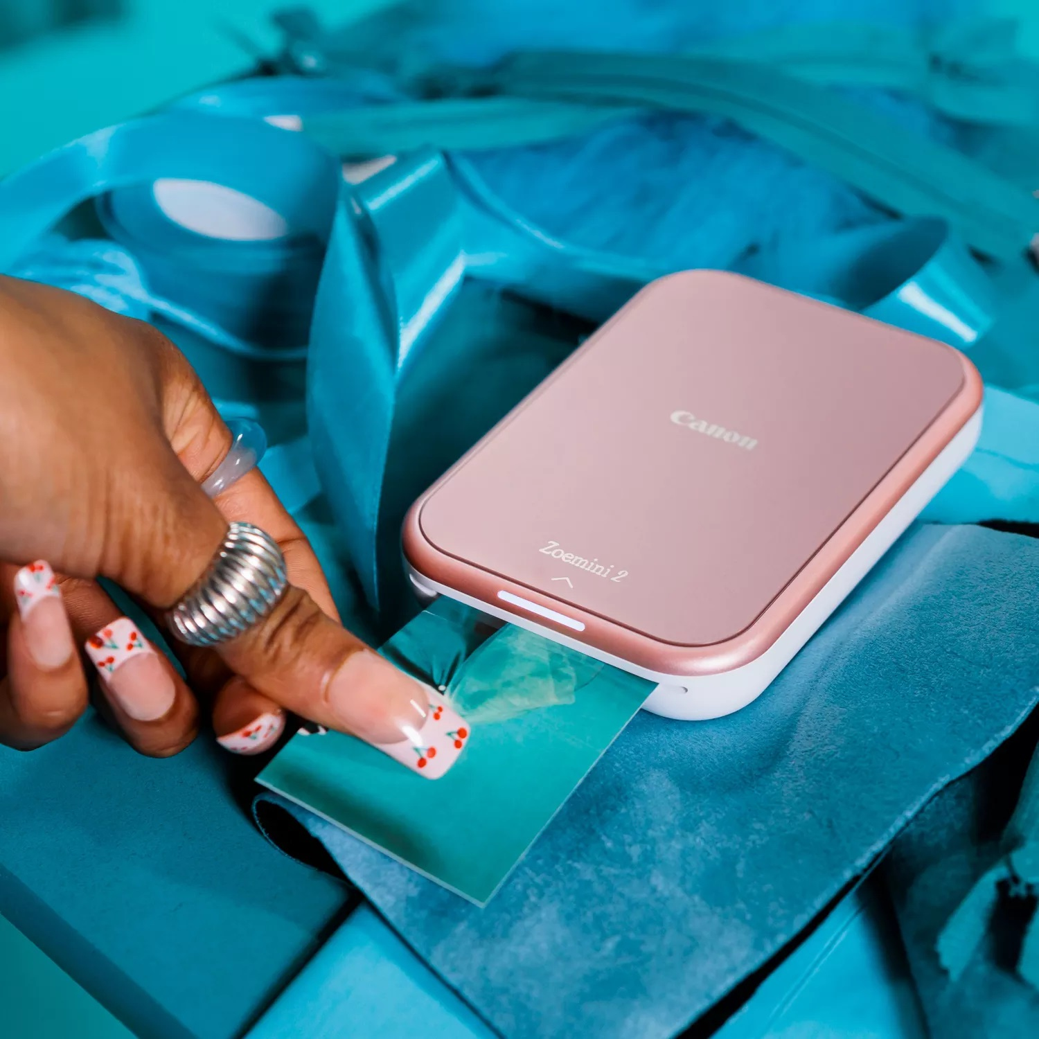 Ręka trzyma zdjęcie z różowego Canon Zoemini 2 na niebieskiej powierzchni.