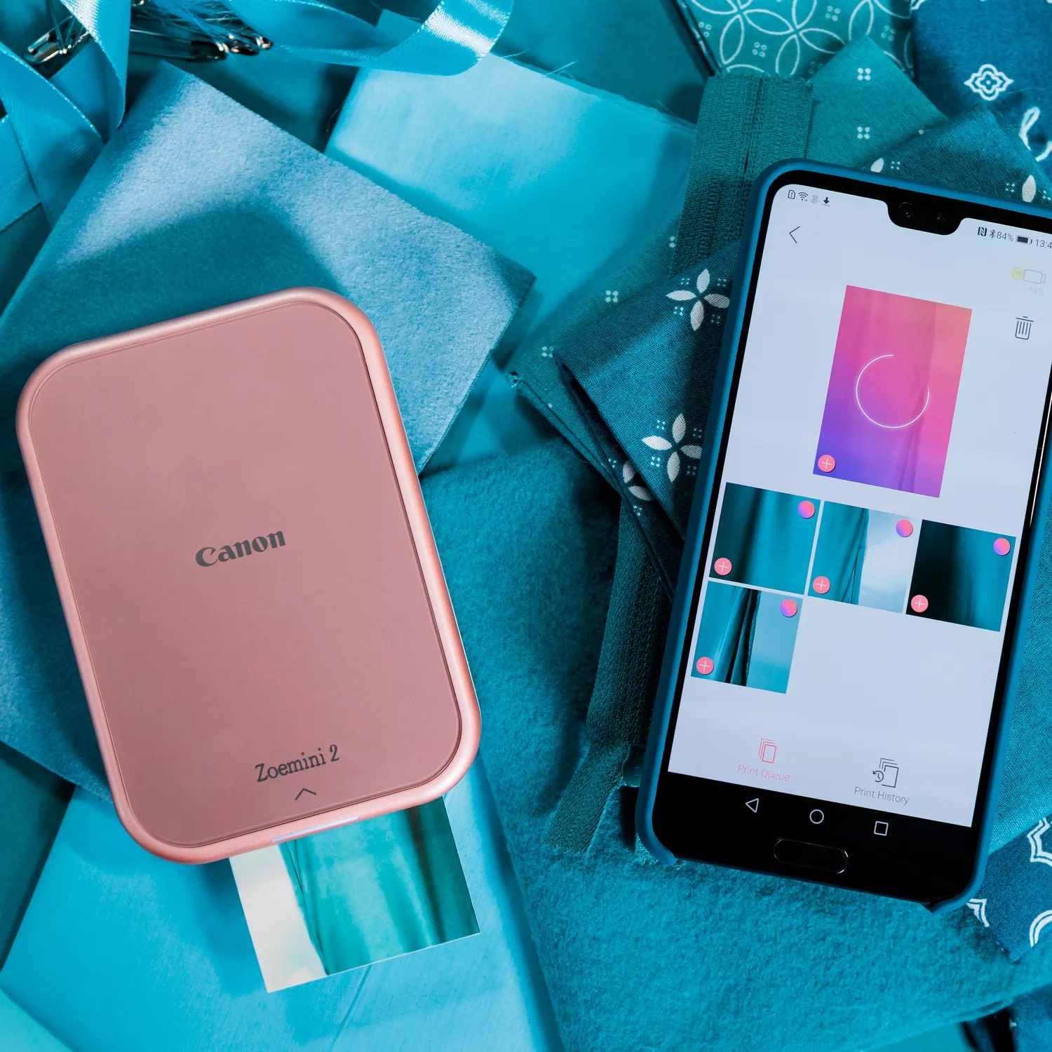 Różowa drukarka Canon i smartfon na niebieskiej powierzchni z tkaniną. Telefon pokazuje zdjęcie.