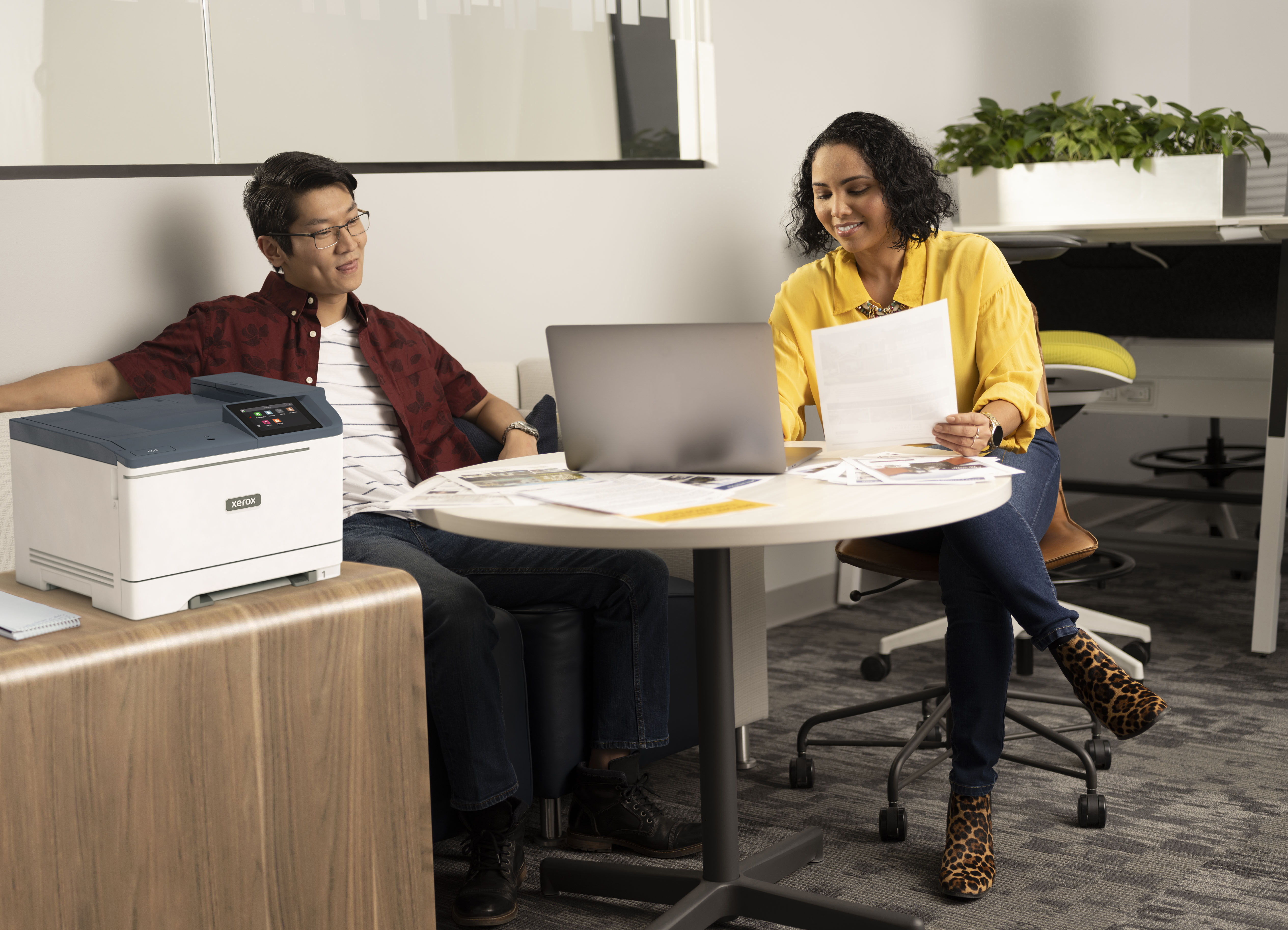 Dwie osoby siedzą przy stole i oglądają papiery, drukarka stoi obok mężczyzny.