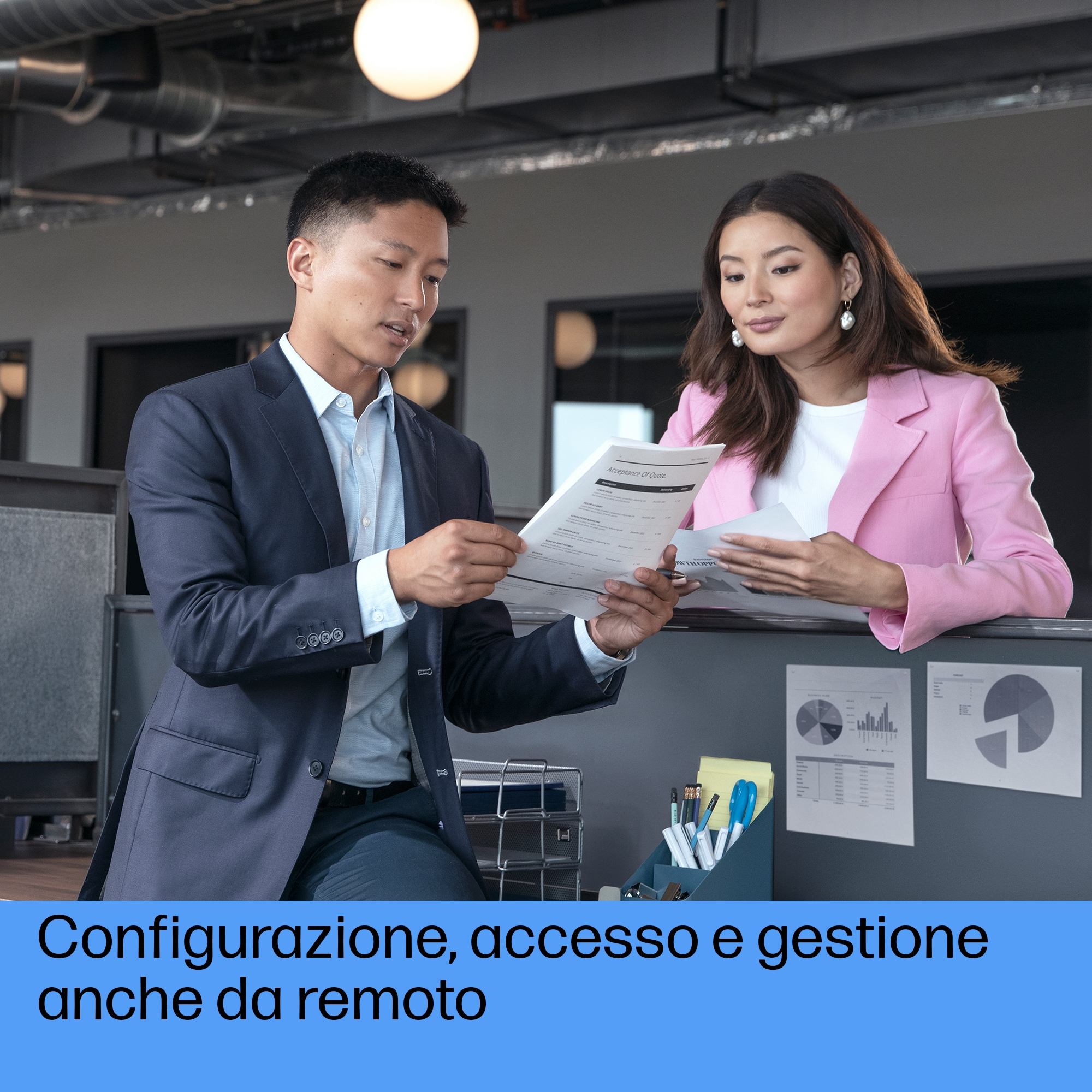 Dwie osoby w biurze przeglądające dokumenty, z wykresami na ścianie i artykułami biurowymi.