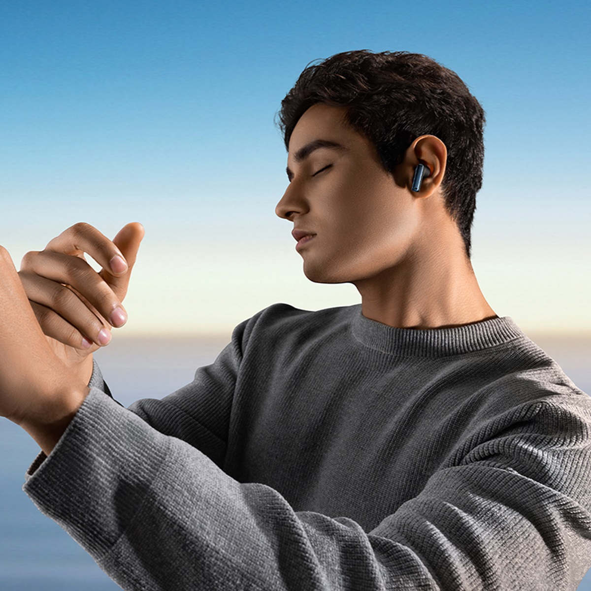 Mężczyzna w szarym swetrze z niebieską słuchawką. Niebieskie niebo w tle.