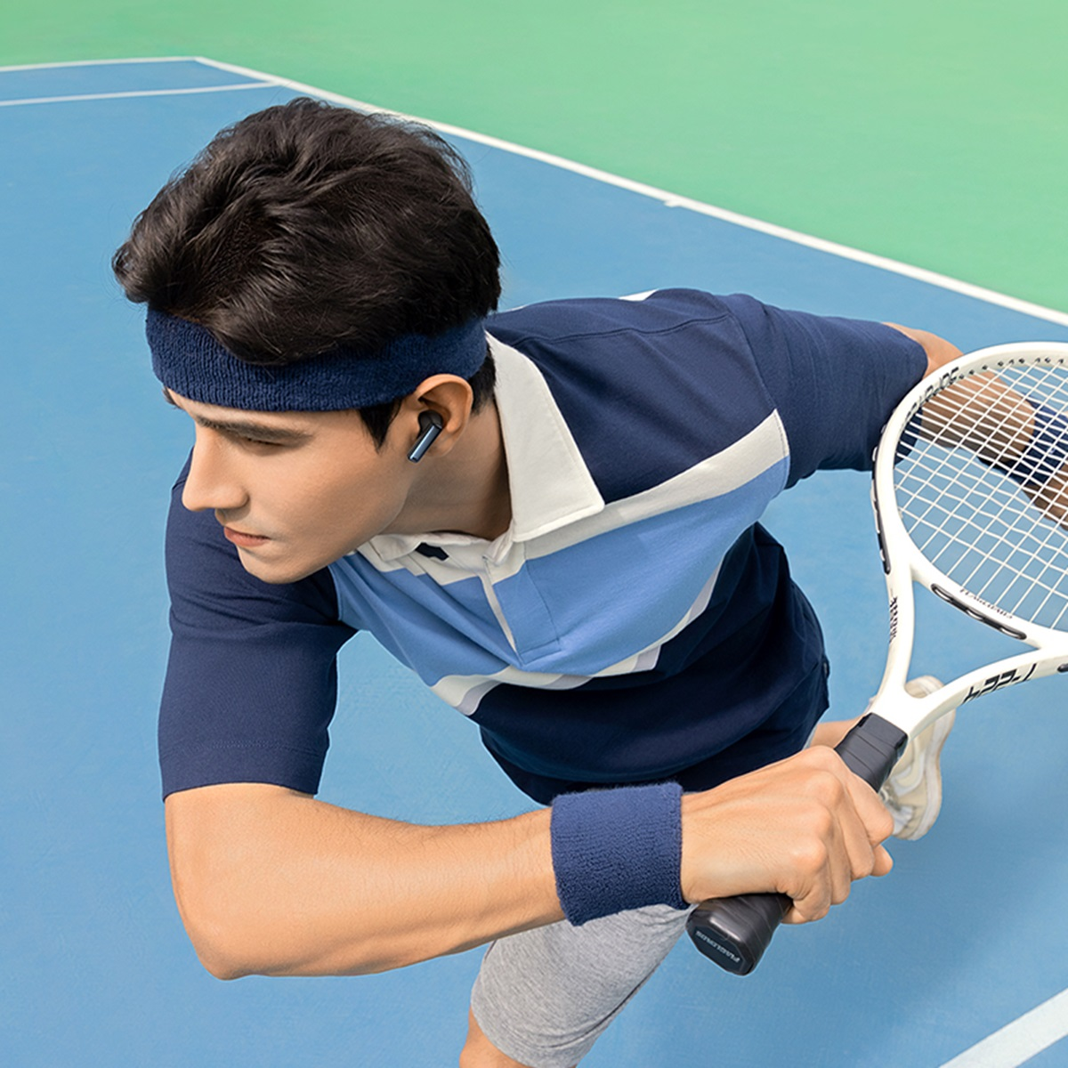 Mężczyzna w niebieskiej koszuli, opasce i opasce na nadgarstek trzyma rakietę tenisową na niebieskim korcie.