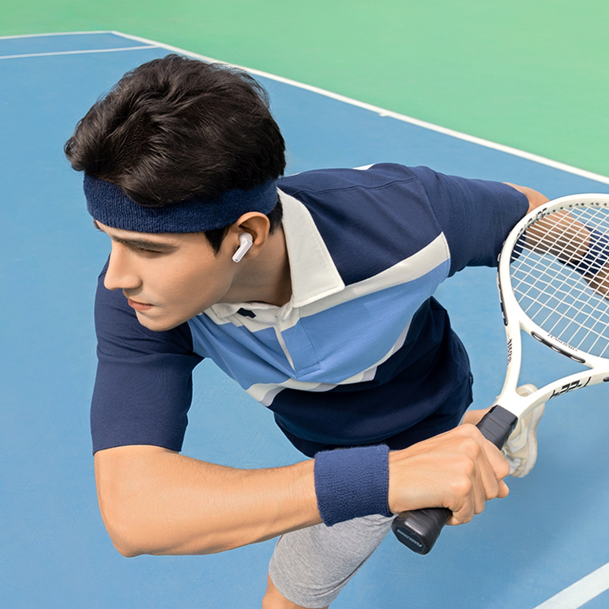 Mężczyzna grający w tenisa, w niebieskiej opasce, koszulce i opasce na nadgarstek, trzymający rakietę.