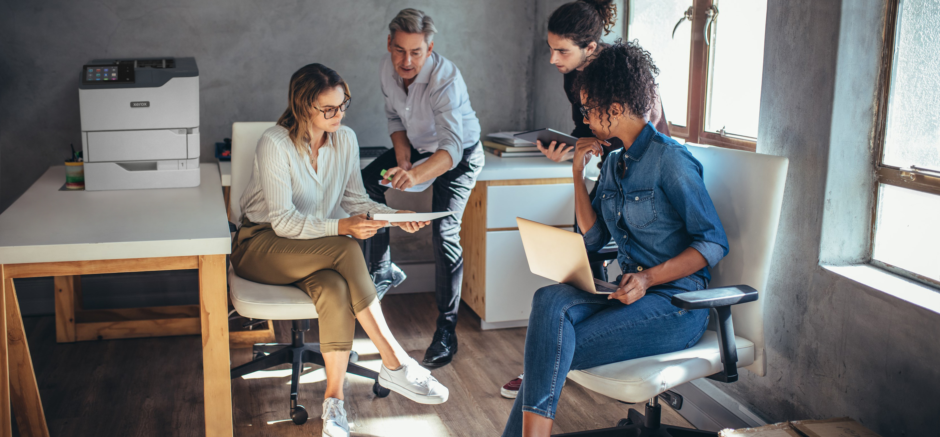 Scena biurowa z ludźmi wokół biurka, drukarka w tle.