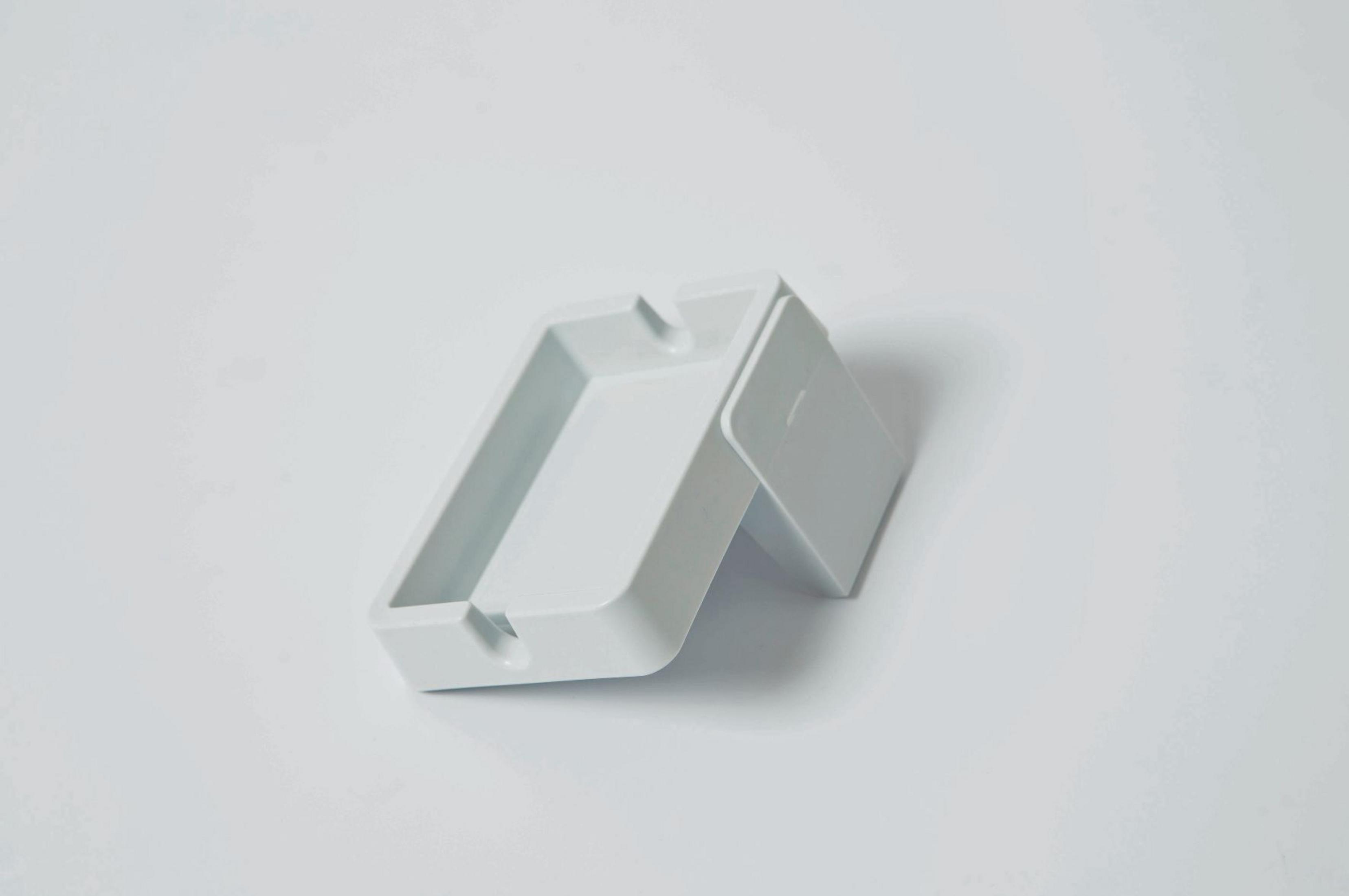 Biała popielniczka na białym tle, z małą, otwartą pokrywą.