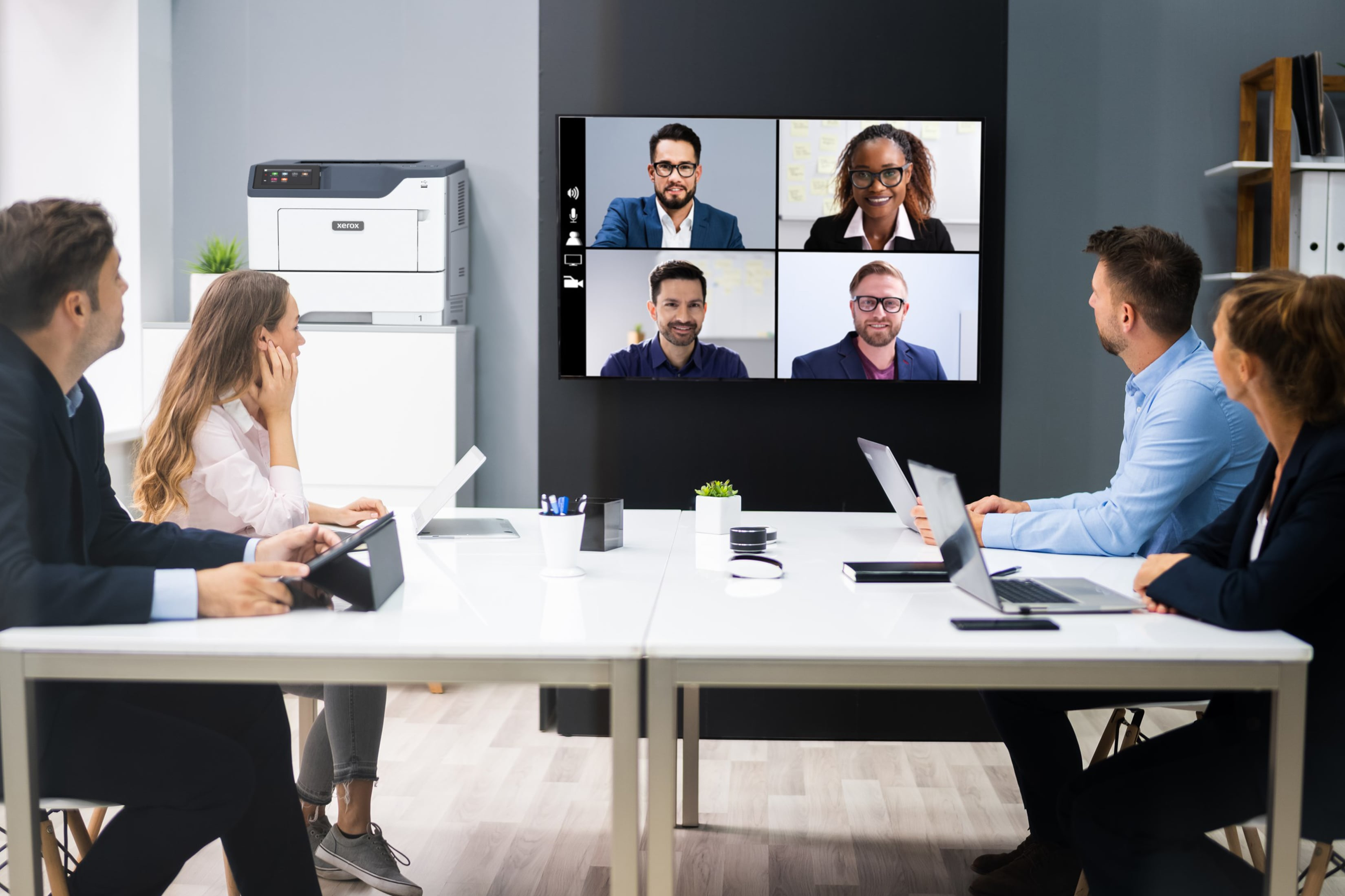 Wideokonferencja na ekranie, pokazująca cztery osoby na spotkaniu. Inne osoby są z przodu.
