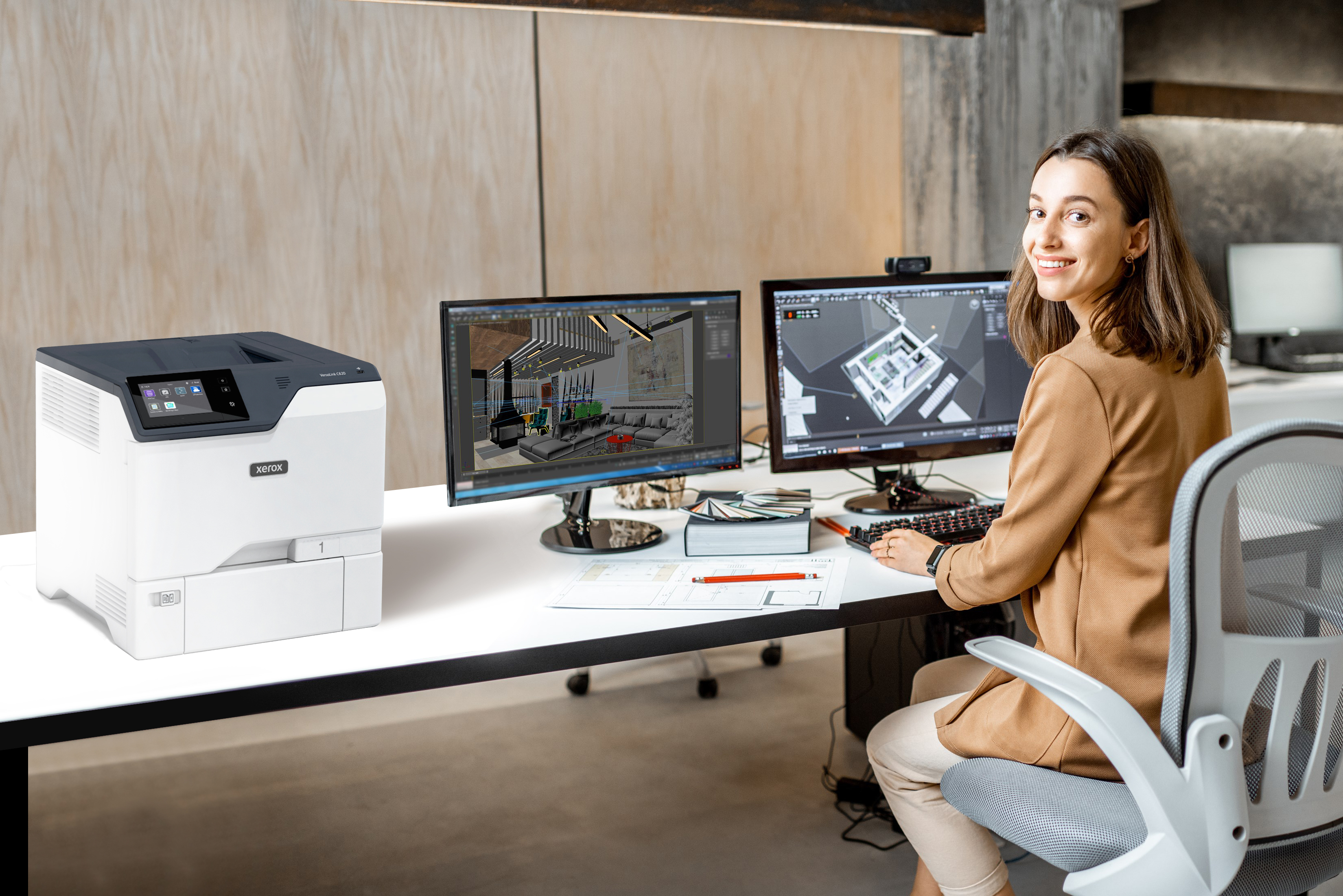 Kobieta przy biurku z dwoma monitorami i drukarką Xerox. Kobieta się uśmiecha, drukarka jest biała.