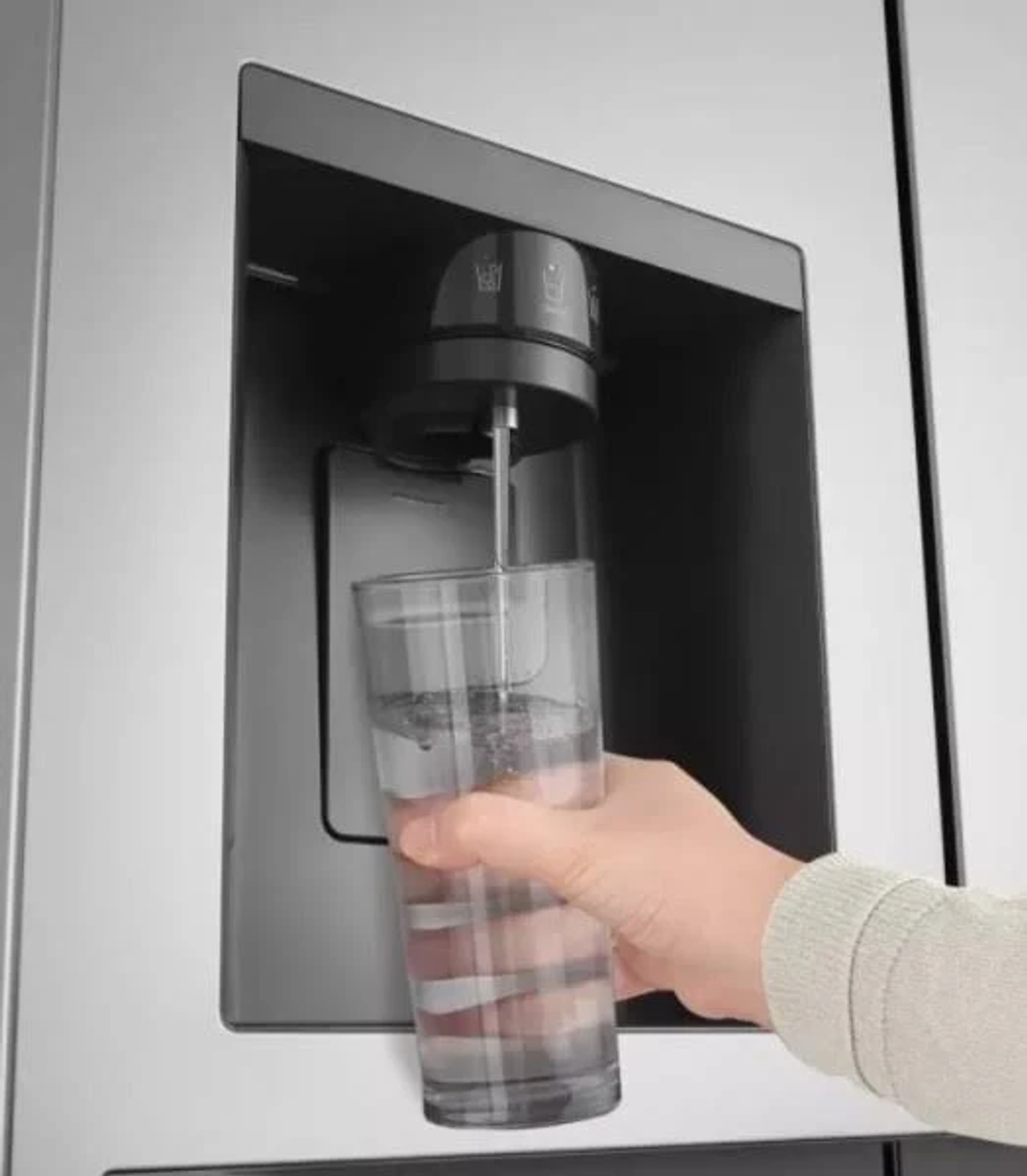 Una mano che tiene un bicchiere che si riempie di acqua da un distributore sulla porta di un frigorifero.